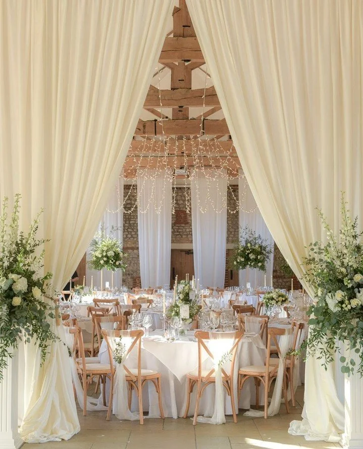 By combining a "Central Apex" scheme with fairy lights, a "Partition Drape" and elegant table styling, a March wedding can feel effortlessly light and fresh. Enhancing the natural tones of the barn while creating a romantic glow f
