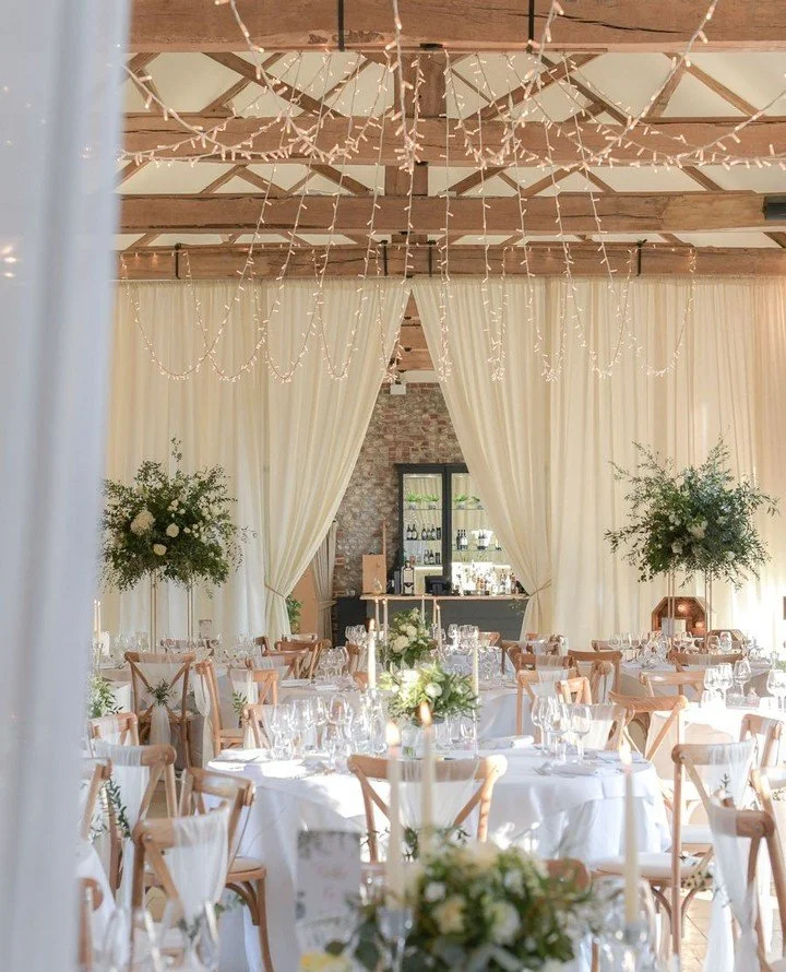 By combining a "Central Apex" scheme with fairy lights, a "Partition Drape" and elegant table styling, a March wedding can feel effortlessly light and fresh. Enhancing the natural tones of the barn while creating a romantic glow f