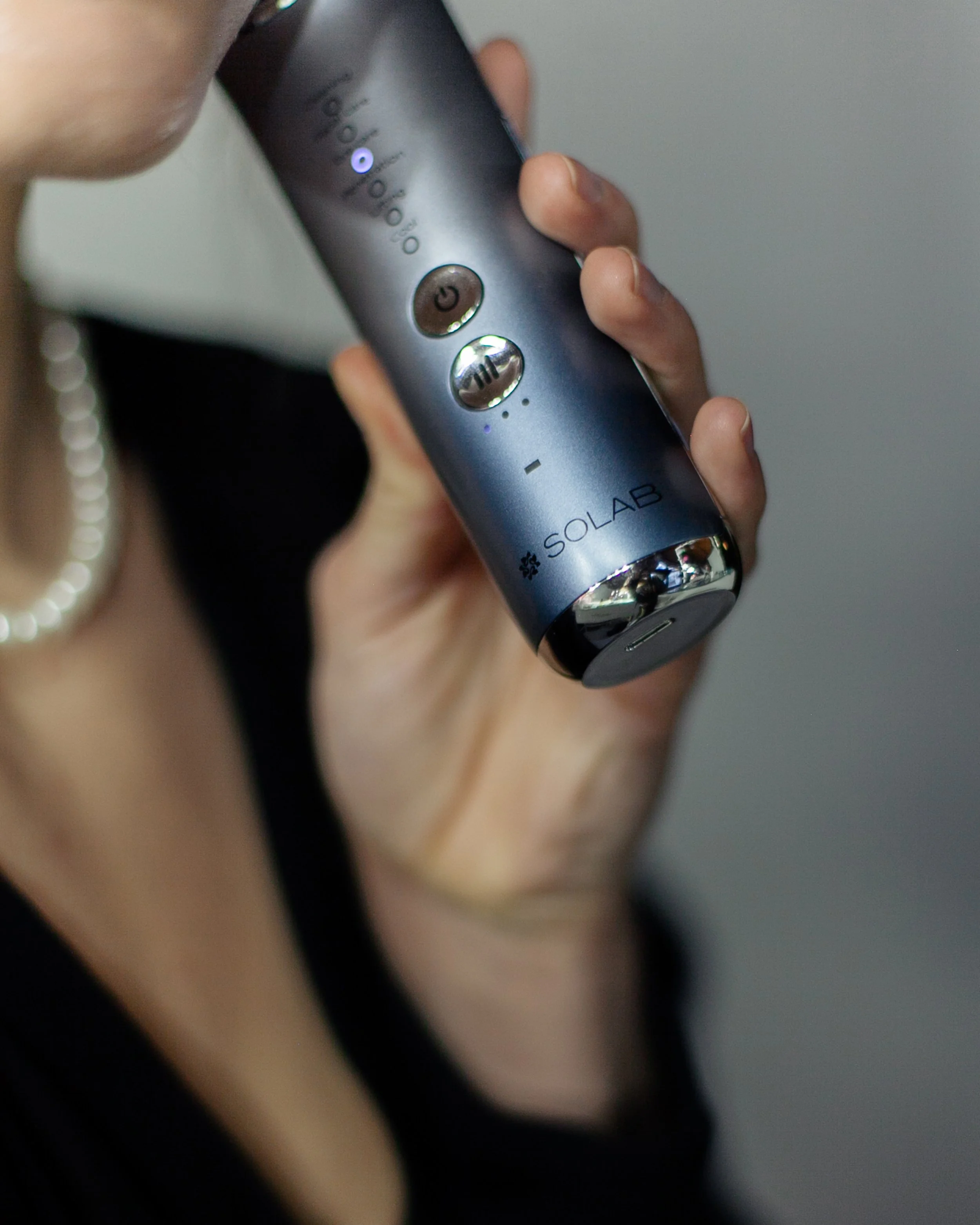 A person holding a gray SOLAB portable vaporizer with buttons and LED lights.