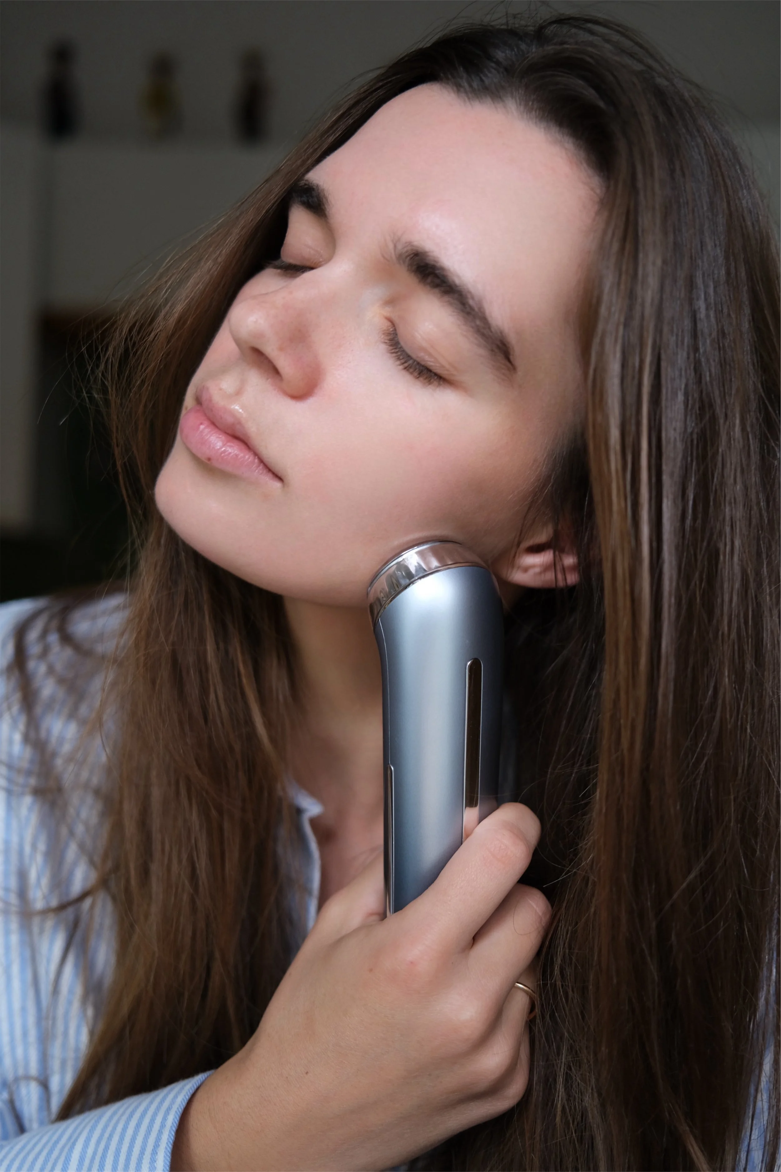 A woman with closed eyes using a facial cleansing device on her cheek.