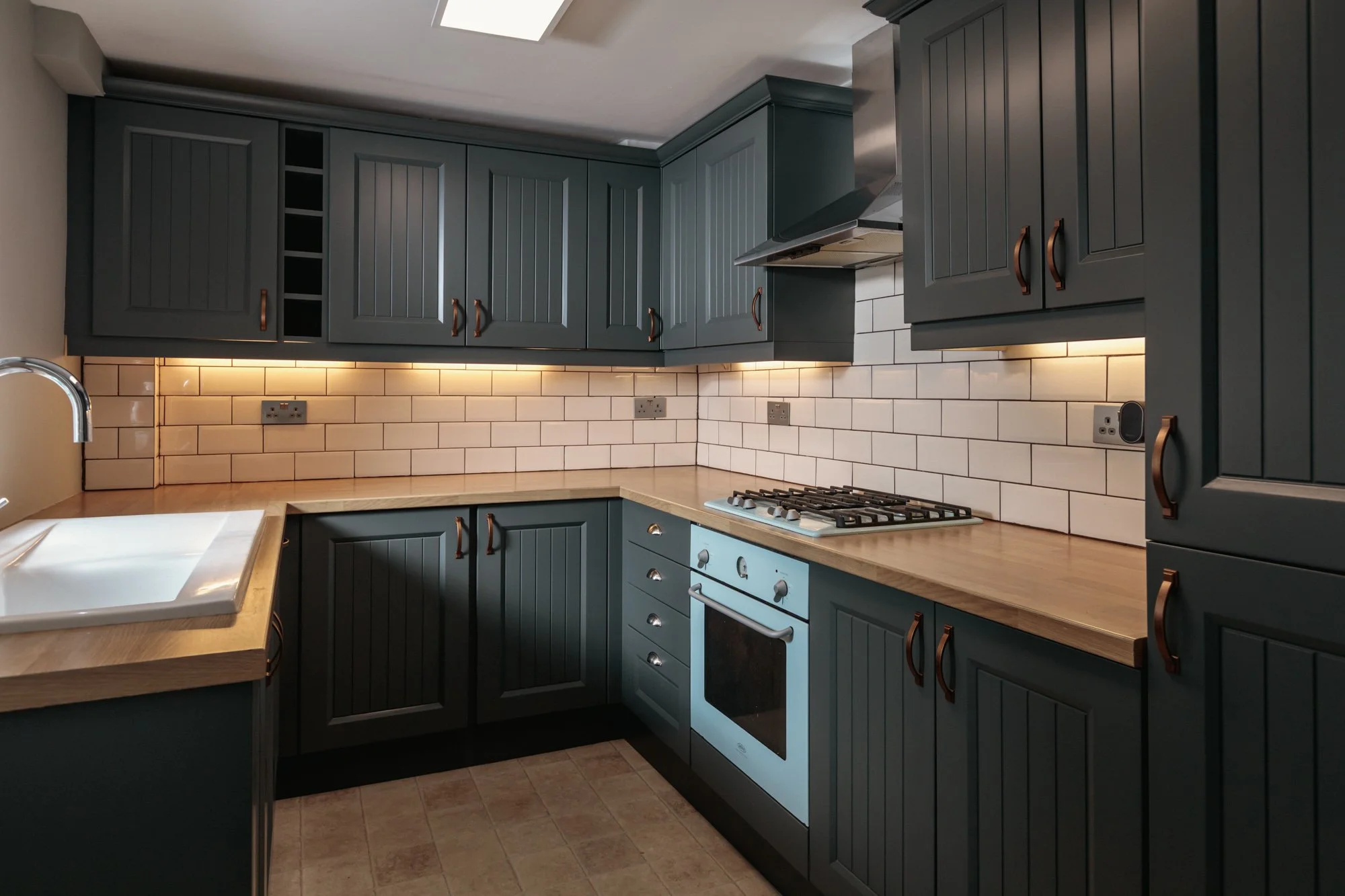 Modern kitchen with dark gray cabinets, cream tiled backsplash, wooden countertops, a white sink, and a built-in oven with stove top.