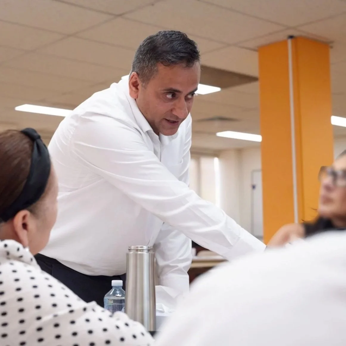 Man in white shirt talking to two women in a meeting room.