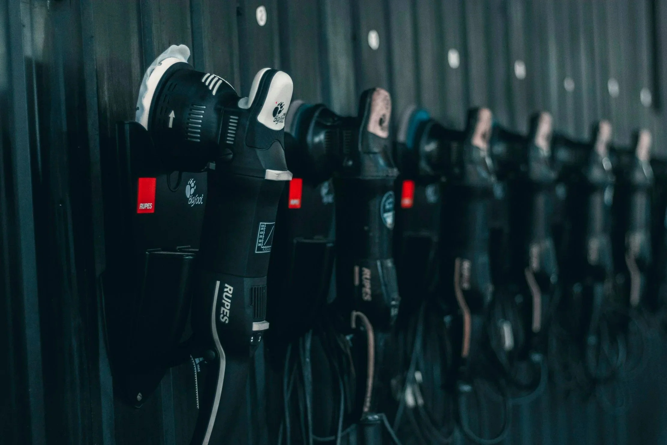 Several polishers hung on a dark wall, arranged in a row.