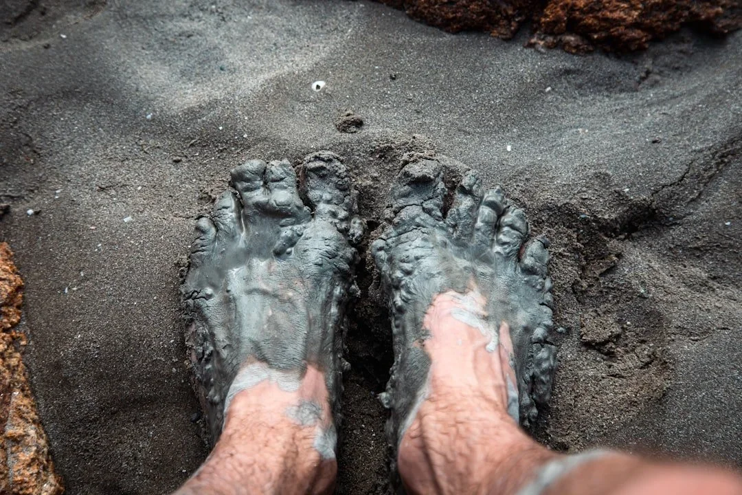 Feet immersed in wet dark gray sand on a beach.