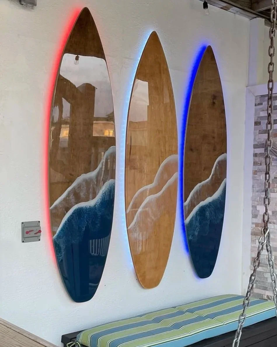 Three oval-shaped mirrors with colored LED lights (red, white, blue) mounted on a white wall, reflecting a beach scene and a person, with a striped bench and chain nearby.
