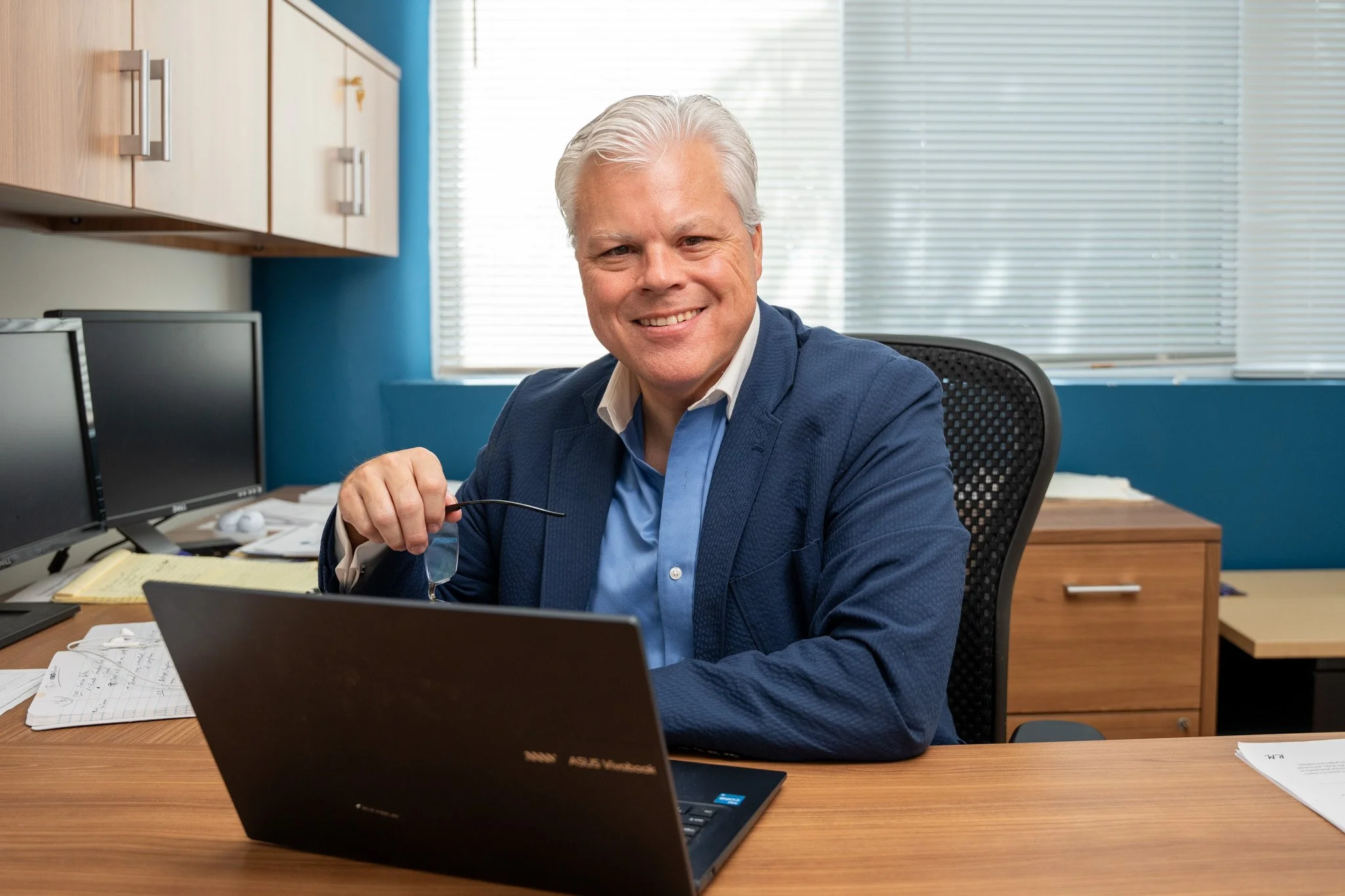 Photo of Bo at his office with a computer and holding his glasses