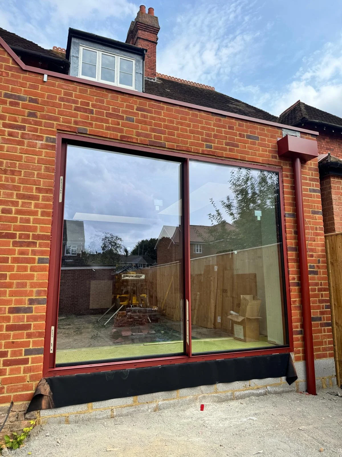 New large glass sliding door installation on a red brick house, with construction materials and tools inside, and a partially finished exterior wall below.