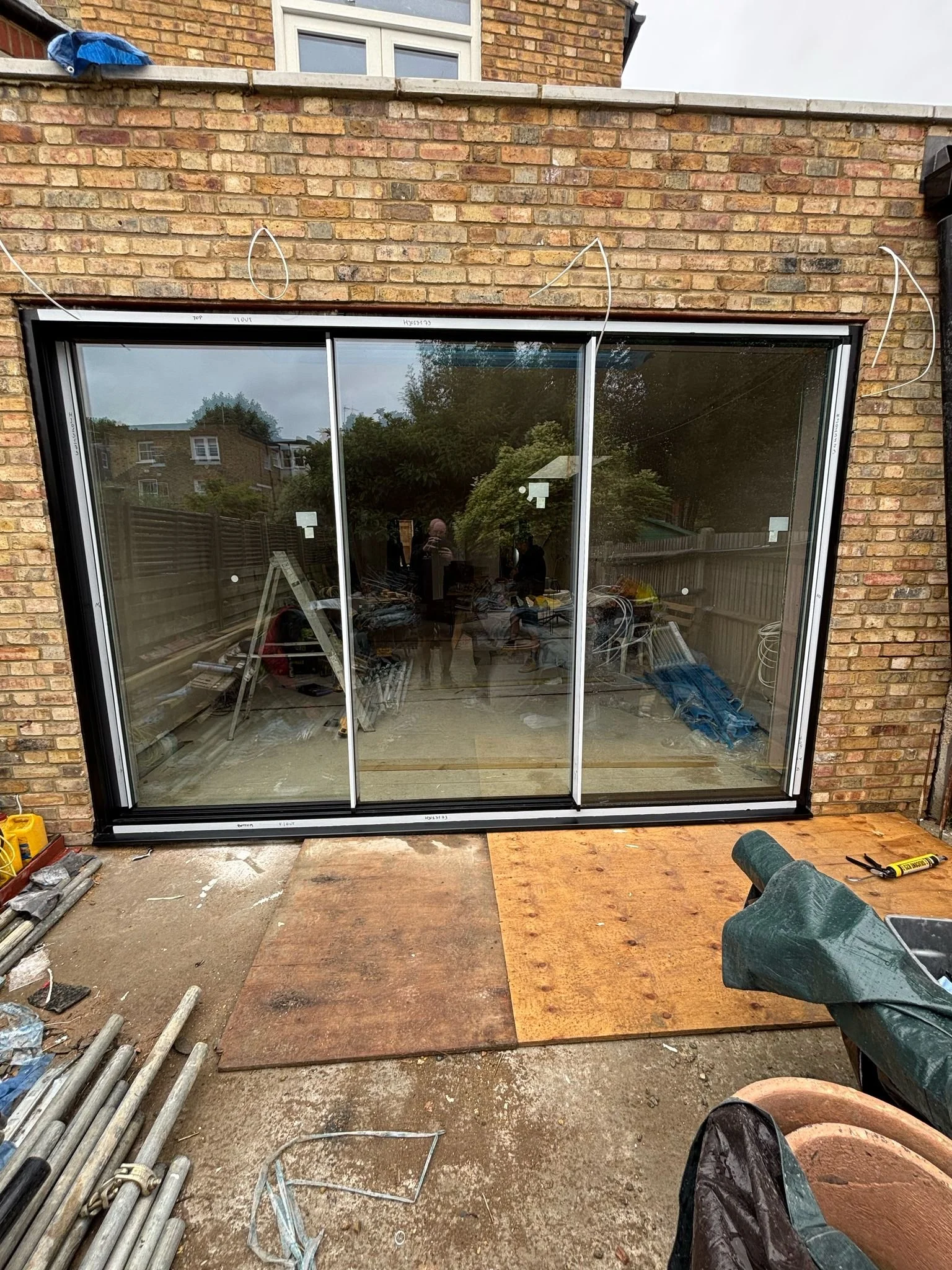 Building a glass sliding door outside a brick house, with tools and construction materials on the ground.