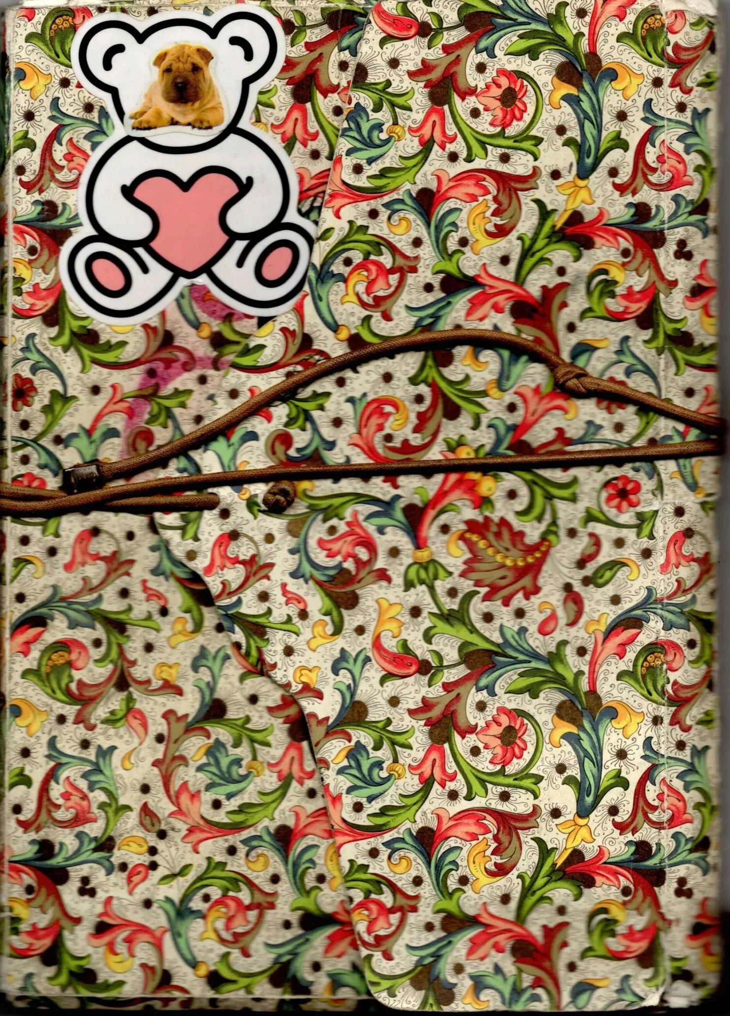 Fondo con patrón floral de colores rojo, verde, amarillo y azul, con una cuerda marrón y una tarjeta decorativa con la imagen de un cachorro de perro en forma de oso y un corazón rosa.