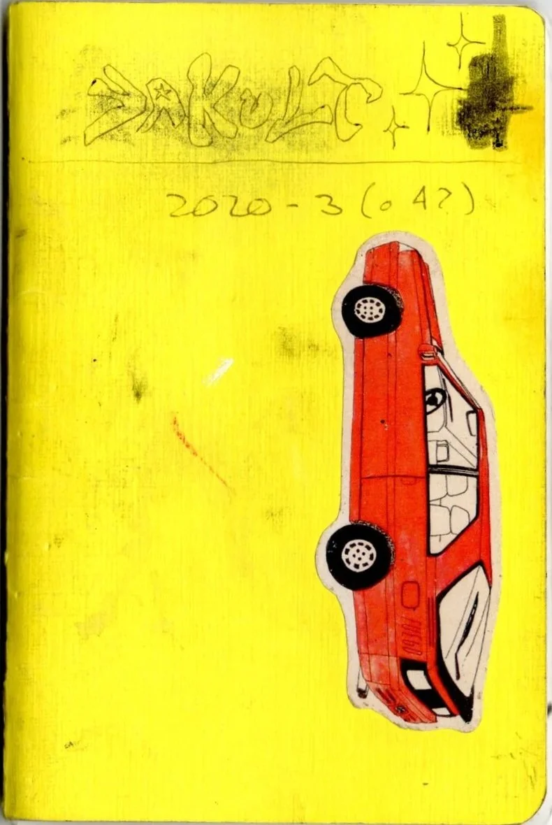 Dibujo de un automóvil rojo en una hoja amarilla con texto escrito y garabatos en la parte superior.