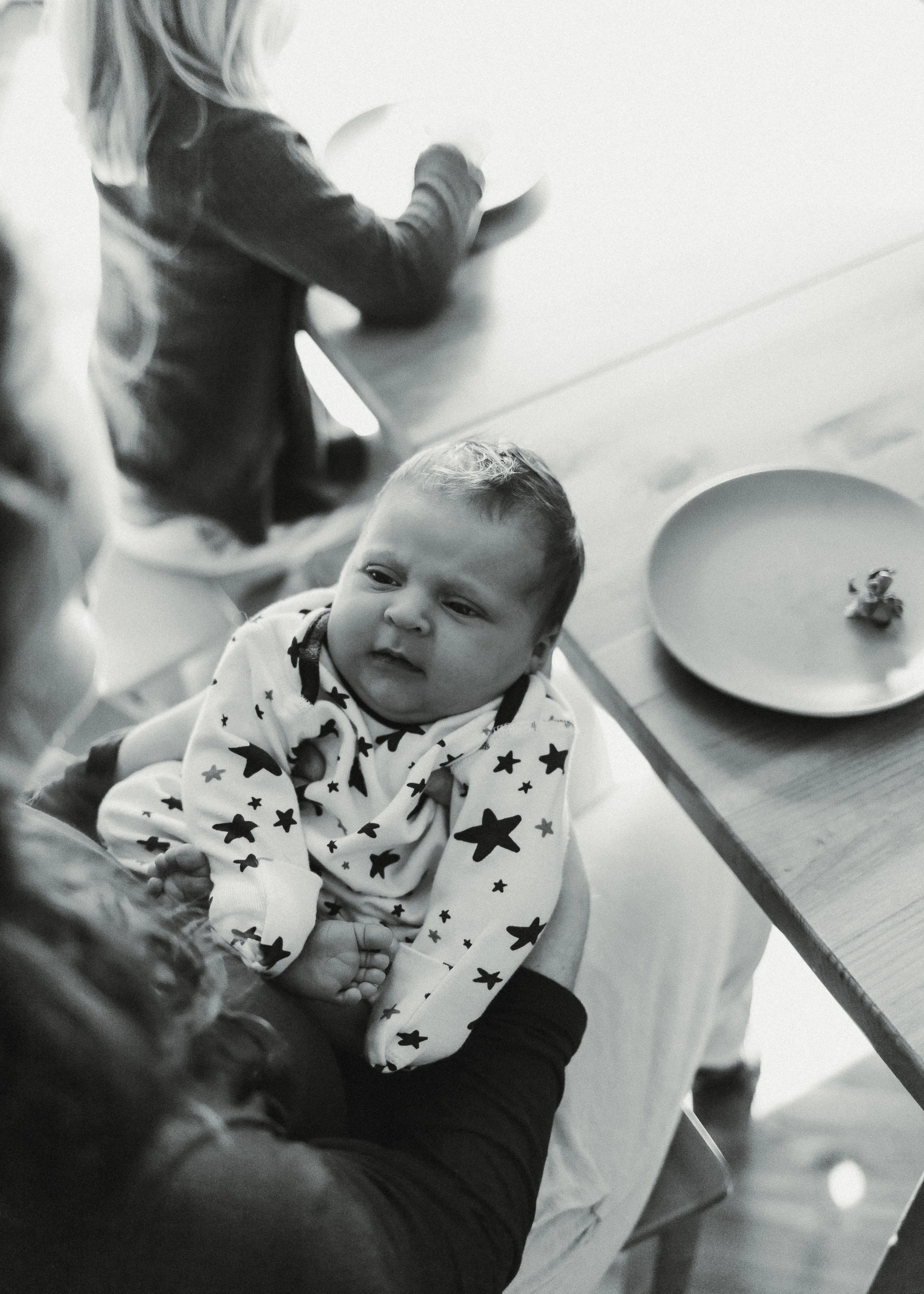 A newborn in a star-printed baby gown is held by her mother, with a plate of chocolate-covered strawberries on a table nearby.