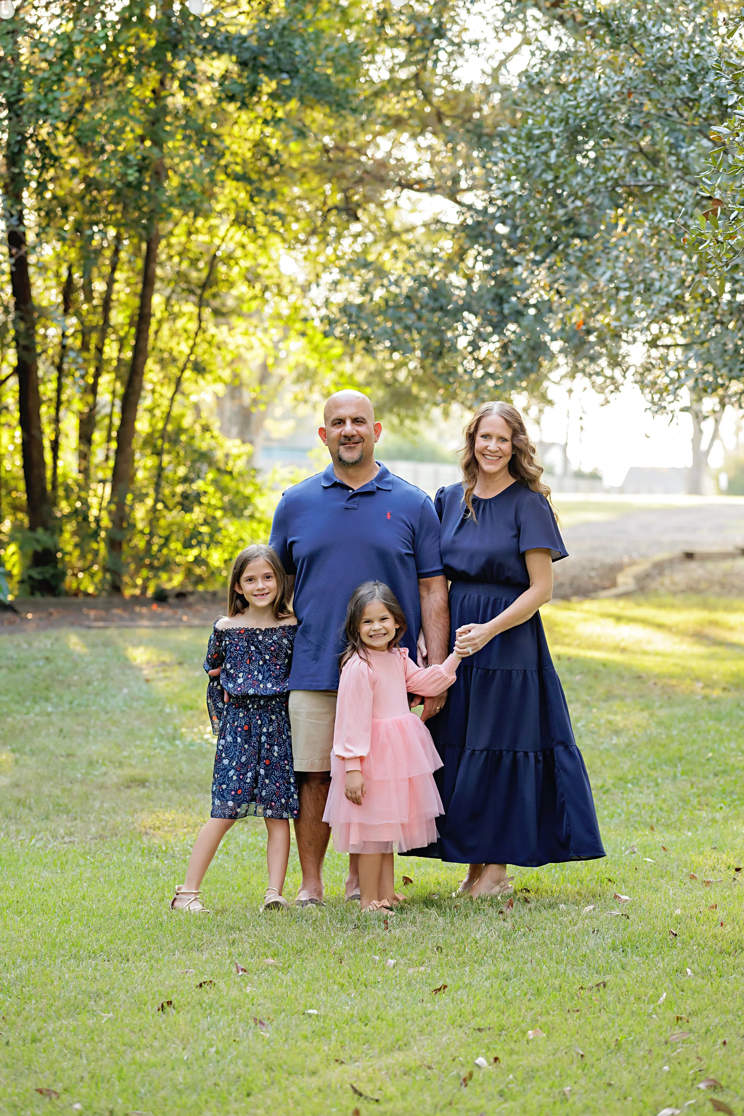 Smiling family in matching outfits, standing together in a sunlit park surrounded by trees and love.