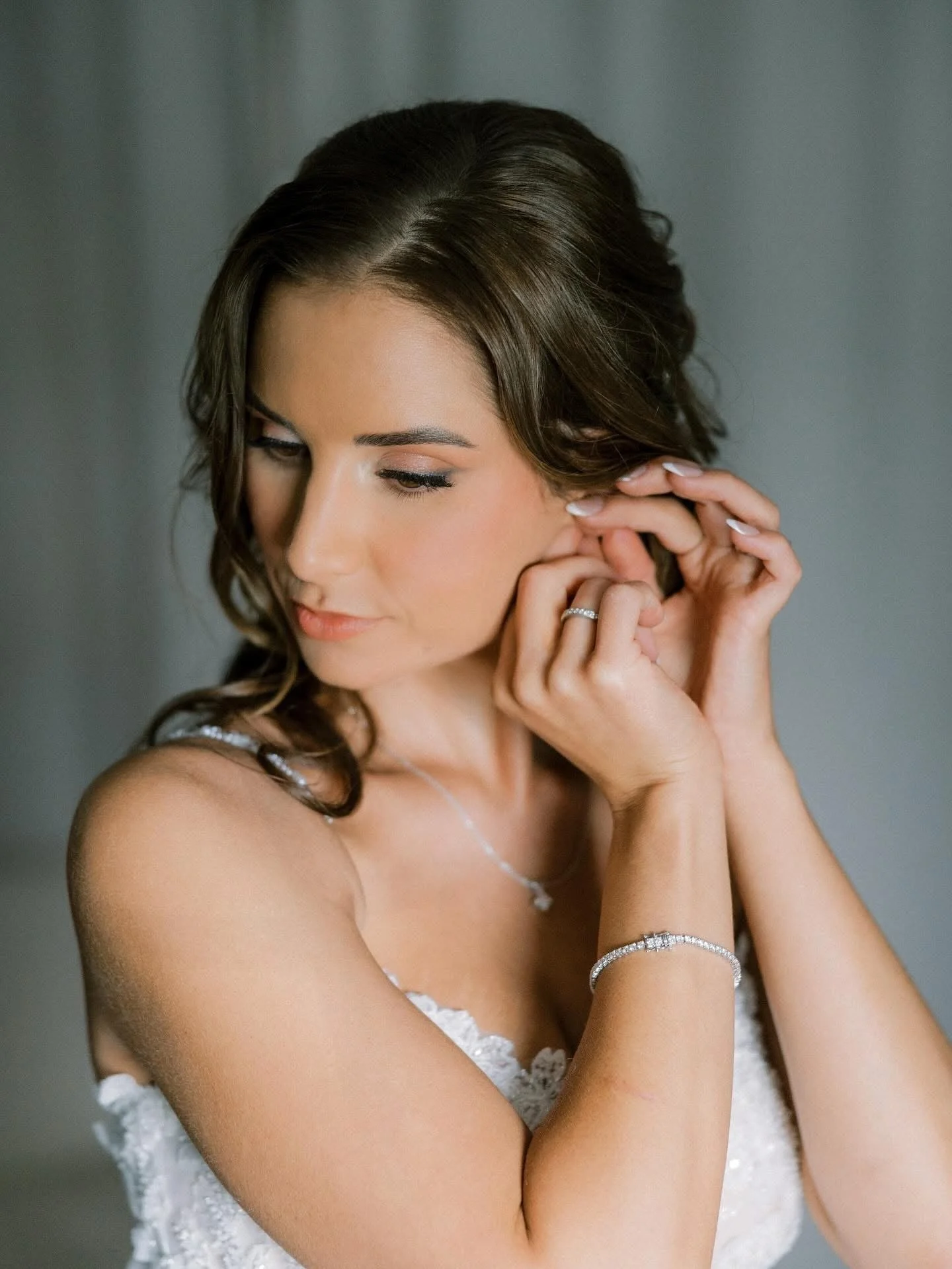 A bride in a white wedding gown holding a bouquet of pink and white flowers, smiling outdoors near a modern building.