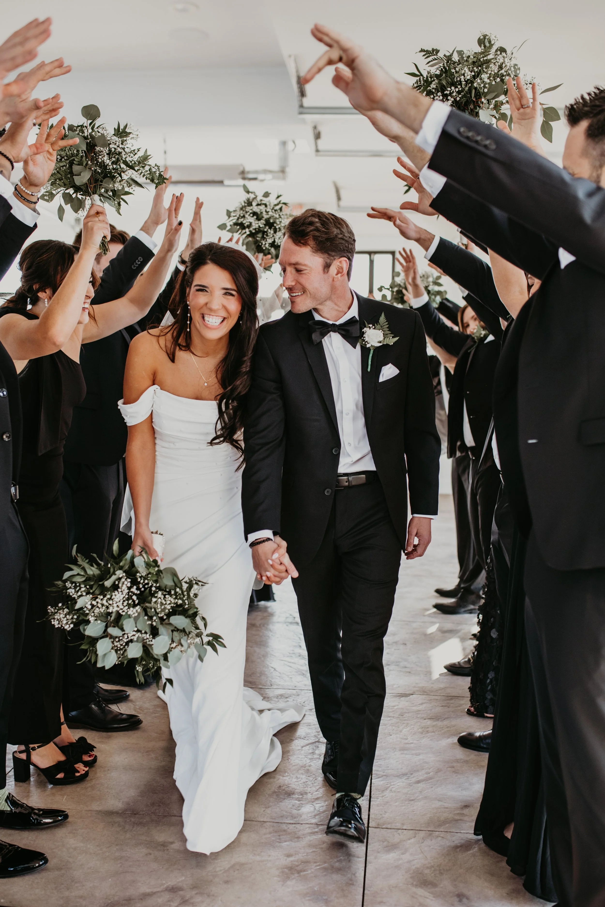 A bride and groom dancing outdoors, under a large tree, with the groom twirling the bride who is smiling. The bride is in a white wedding gown, and the groom is in a black tuxedo.