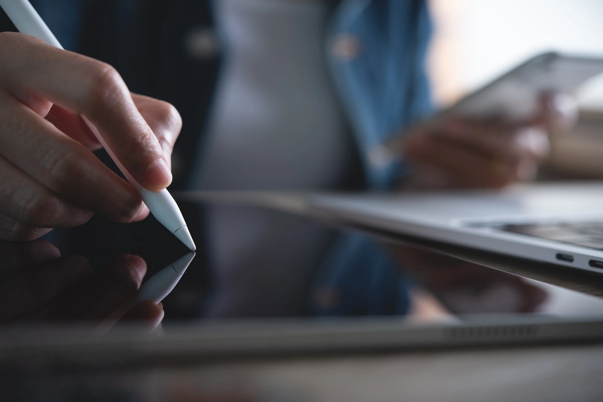 A designer creating digital learning content using a tablet, stylus, and laptop..