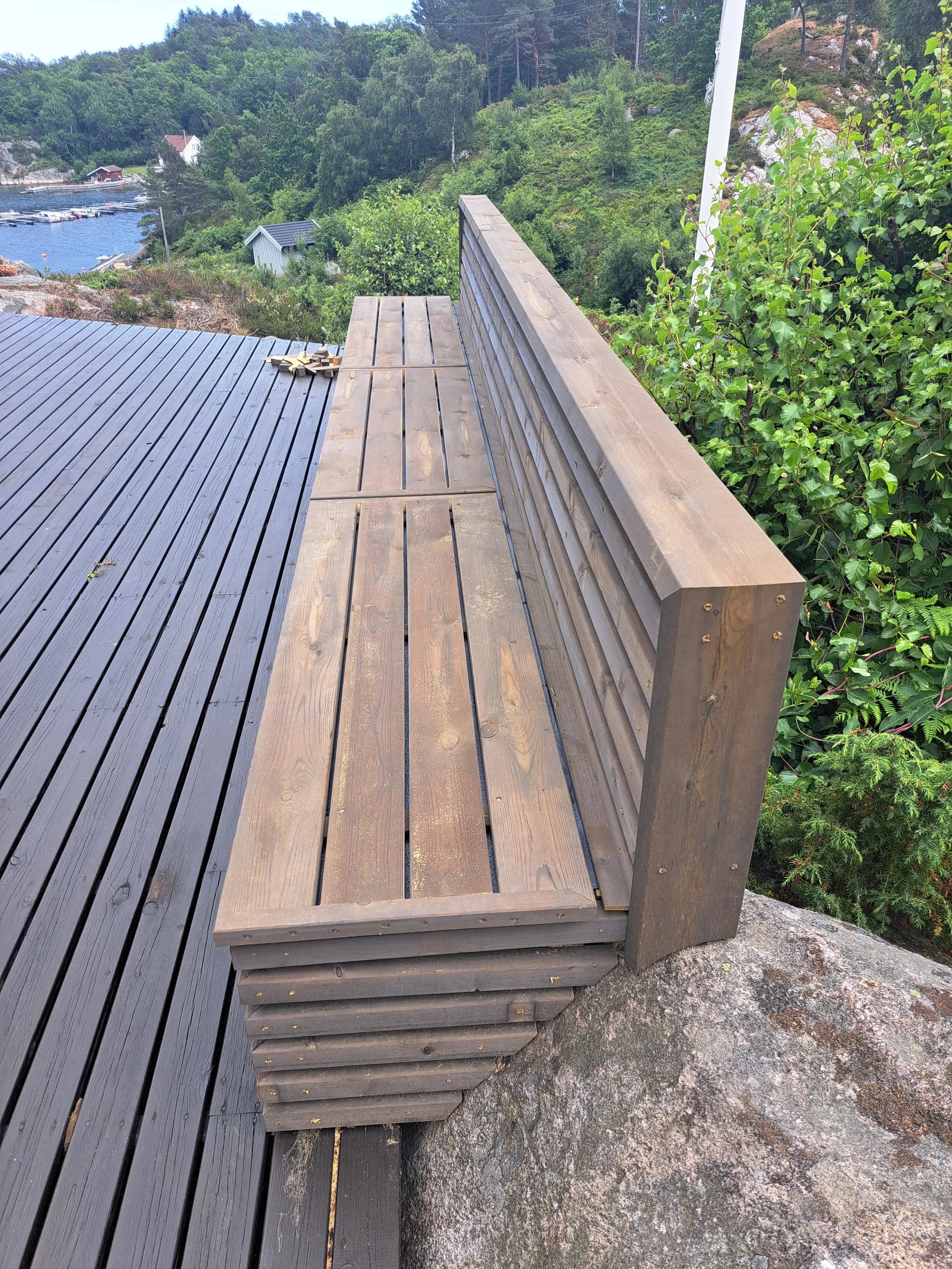 En trebenk på en utsiktsplatå med utsikt over sjø og bygninger i en skogkledd landskap