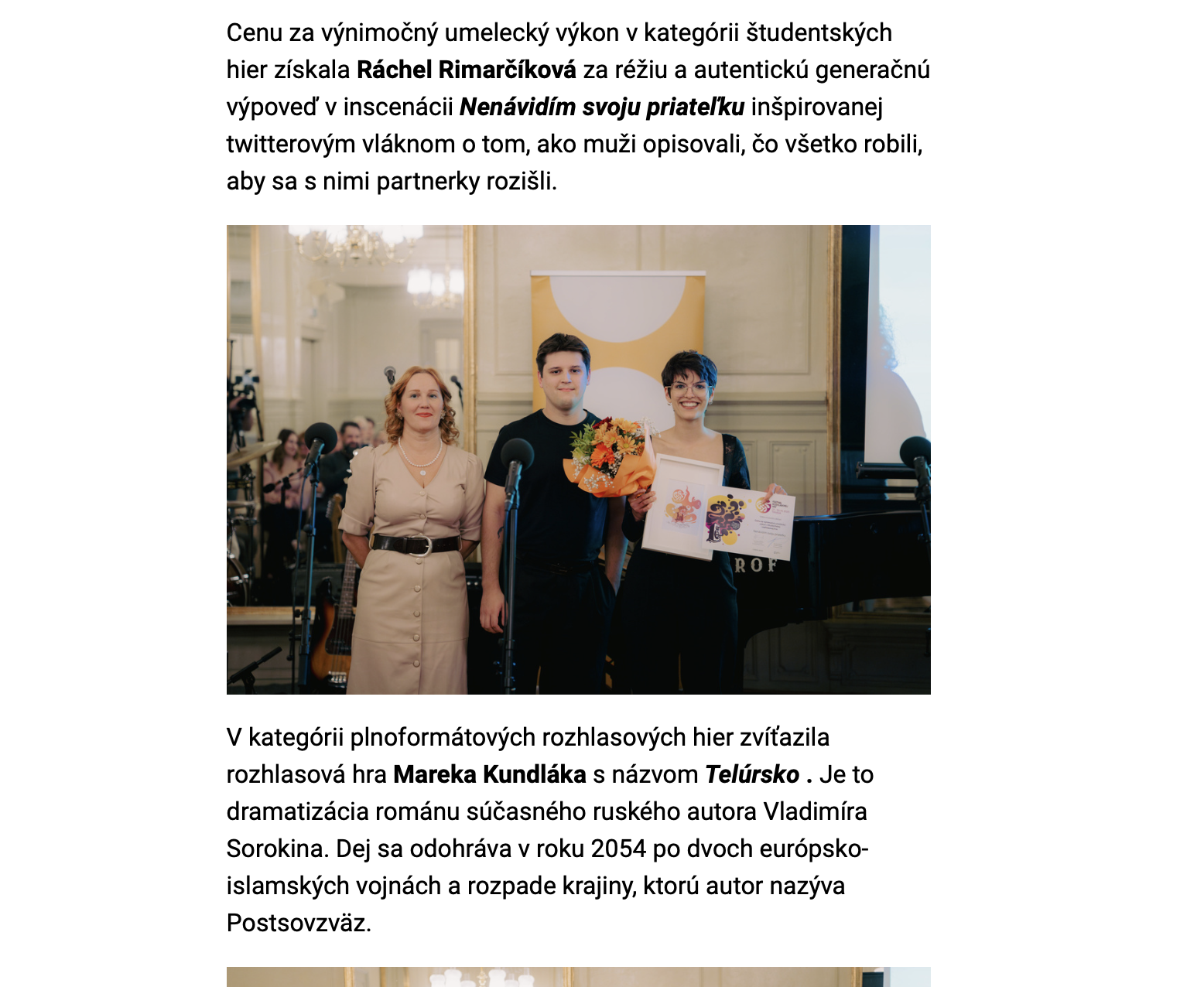 Three women and one man standing onstage at an awards ceremony. The woman on the right holds a bouquet of flowers and a certificate, while the woman on the left is standing behind a microphone. The background features mirrors, chandelier lighting, and a grand room setting.