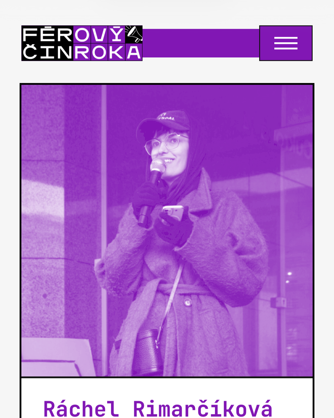 A woman with glasses, wearing a hat and coat, holding a microphone and a phone, standing outside with a background of glass windows and a stone wall.