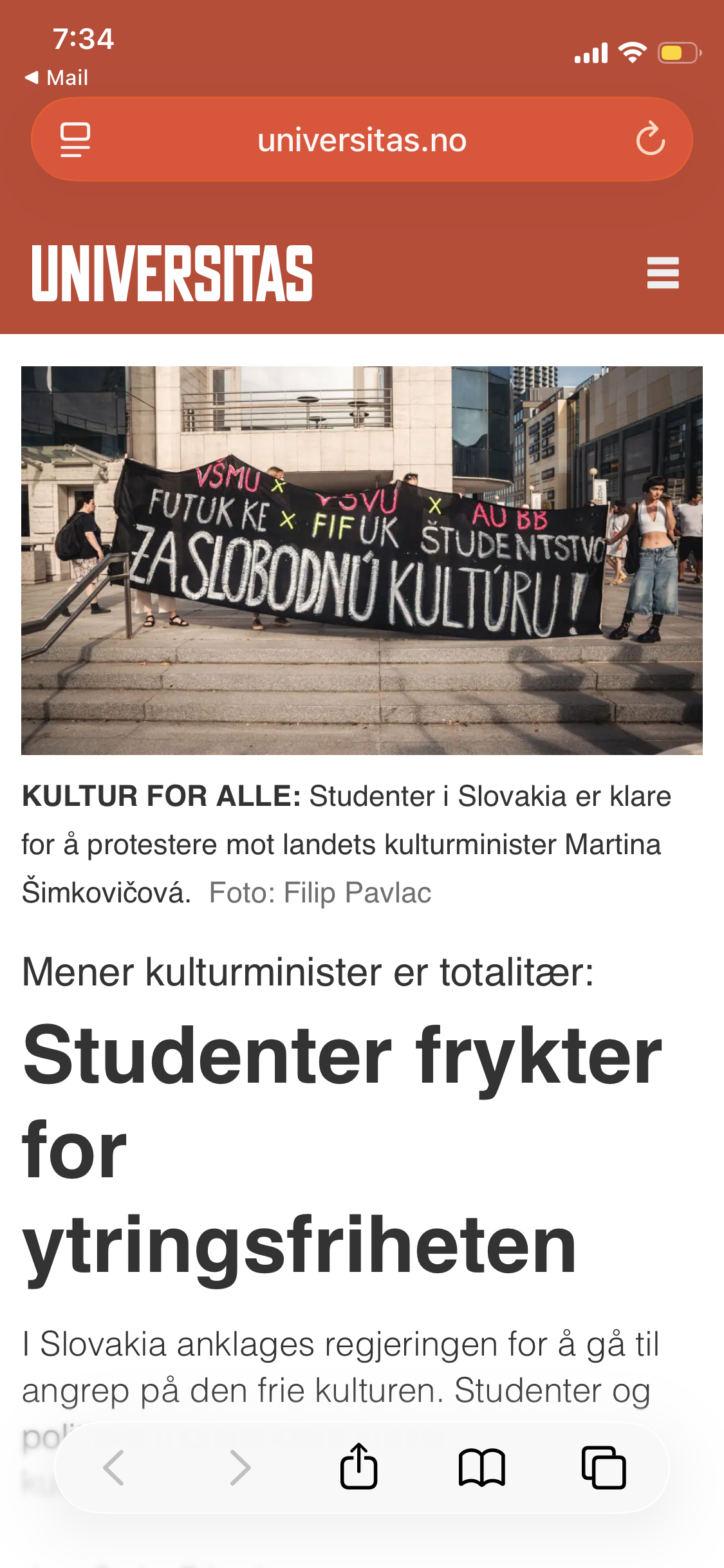 Protesters holding a large black banner with white and neon-colored writing, standing outdoors in an urban area.
