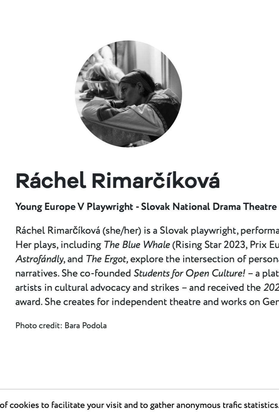 Black and white portrait of a woman resting her head on a table, with several other people in the background.