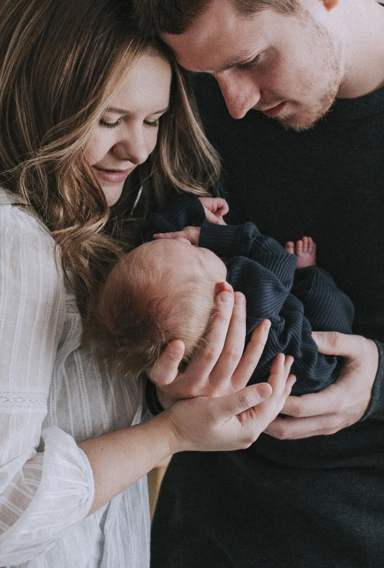 A young couple holding a newborn baby together, gazing lovingly at the infant, indoors.