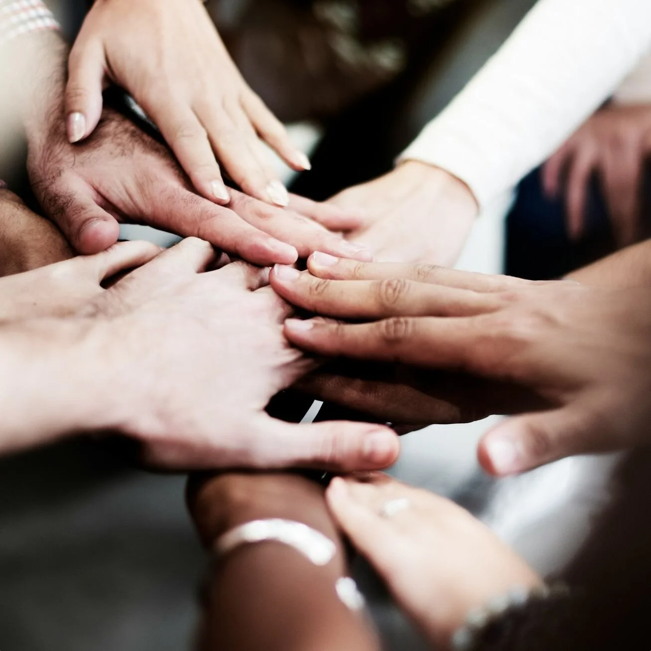 Multiple hands from diverse individuals placing their palms together in a unified gesture.