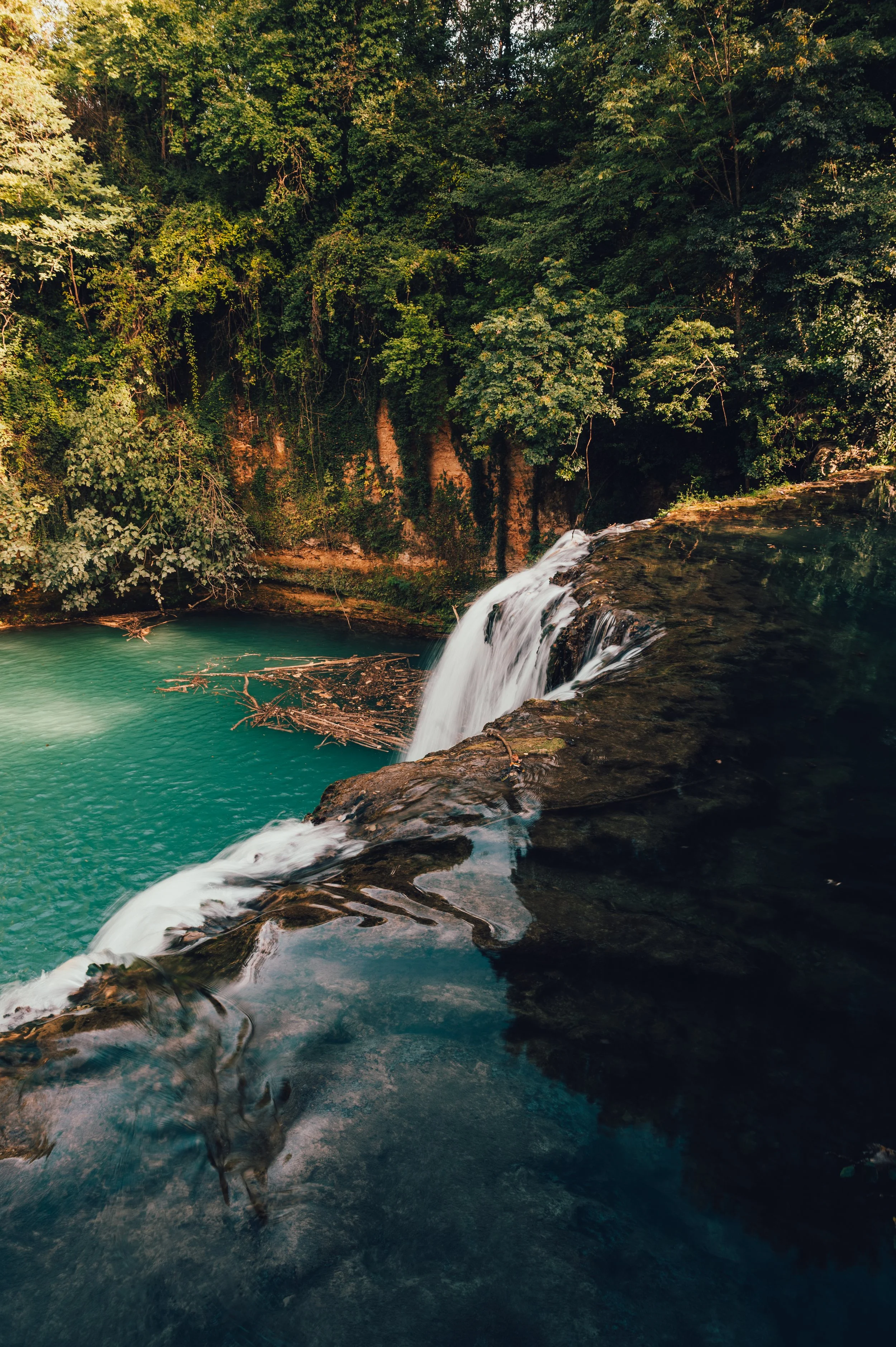 A small waterfall flowing into a turquoise pool surrounded by dense green foliage.