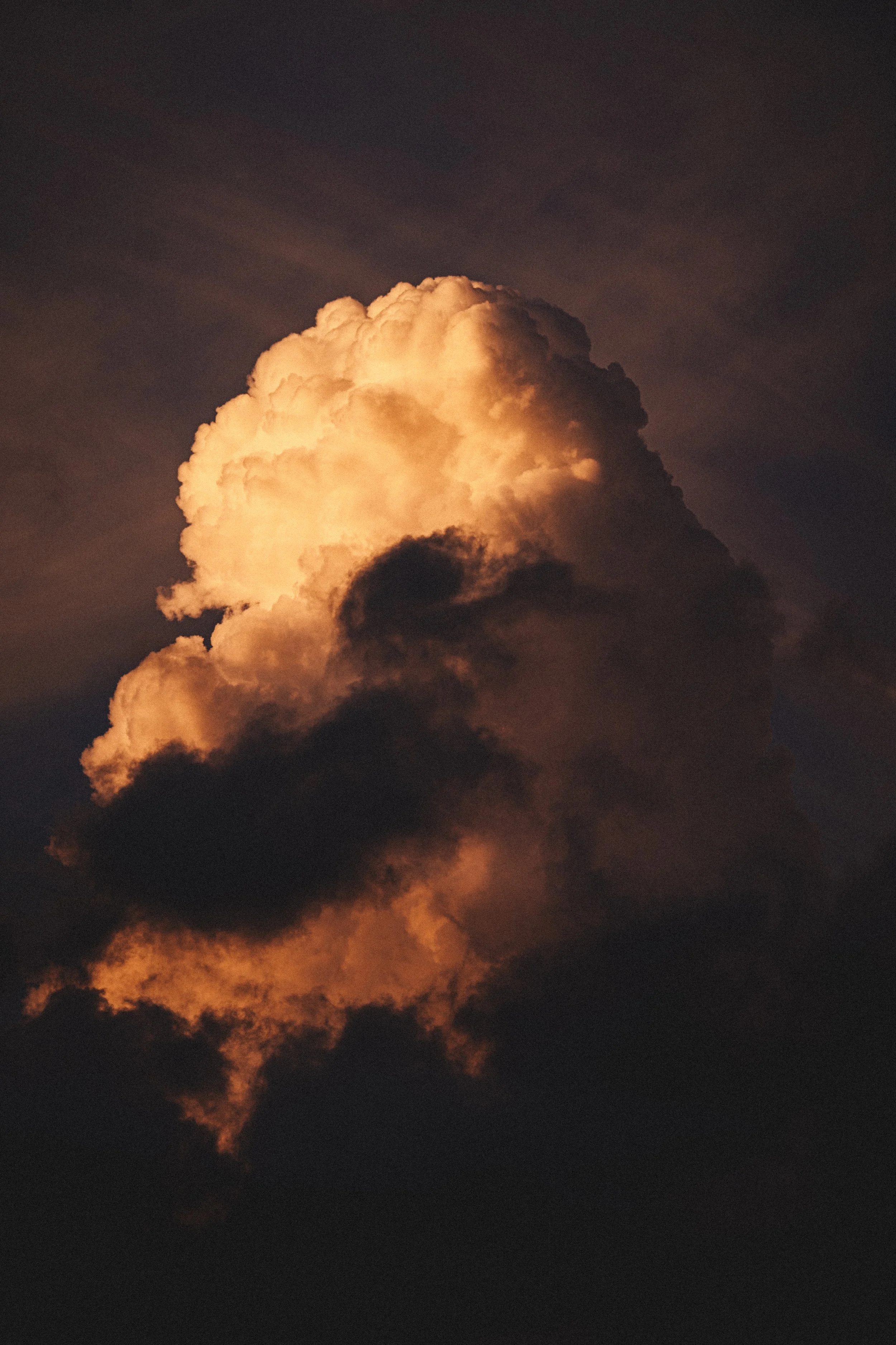 A large cloud illuminated by the setting or rising sun, with dark shadows and a warm glow.