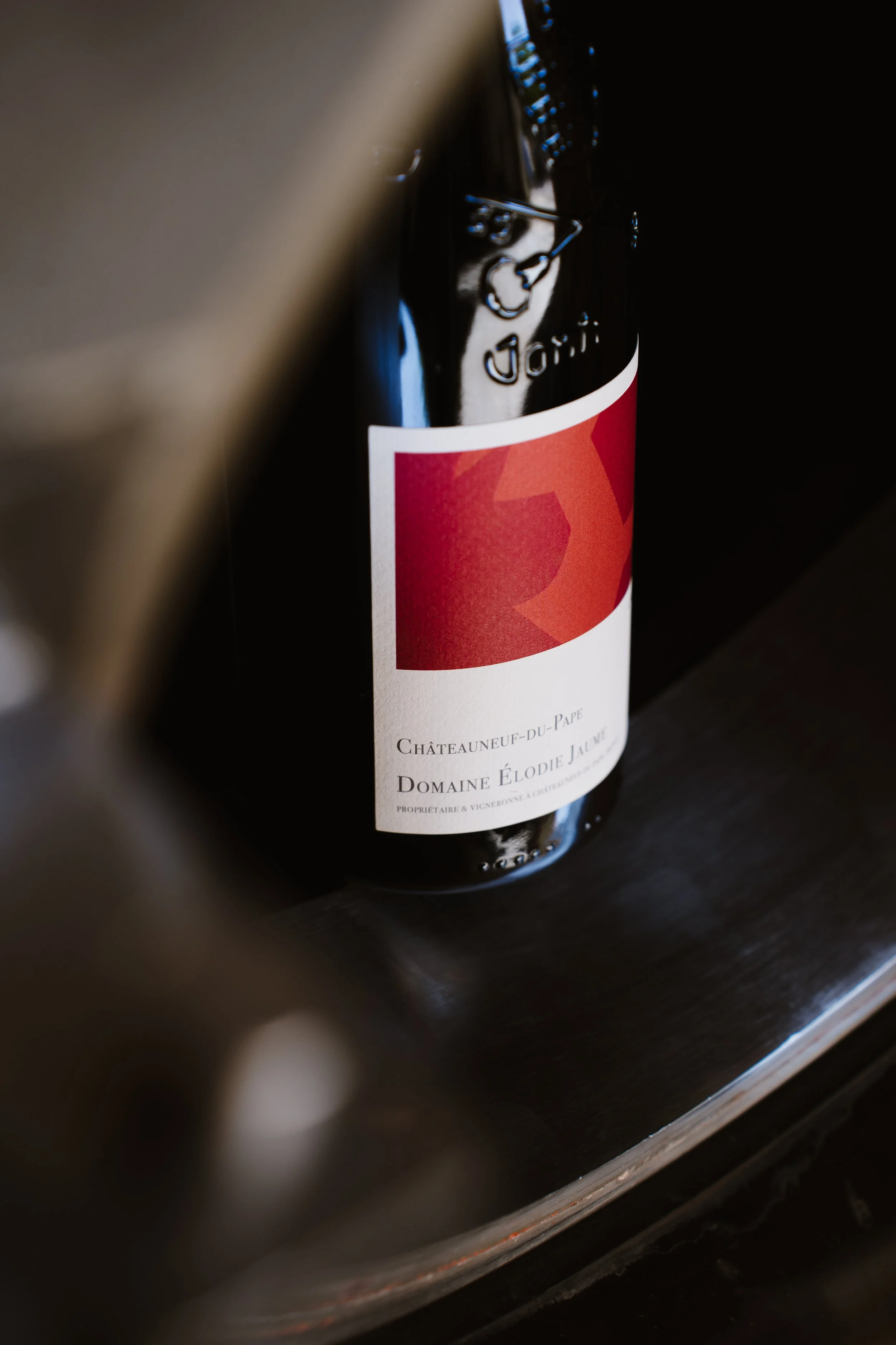 A bottle of red wine from Domaine Elodie Jalmé, Châteauneuf-du-Pape, partially obscured by a blurred object in the foreground.