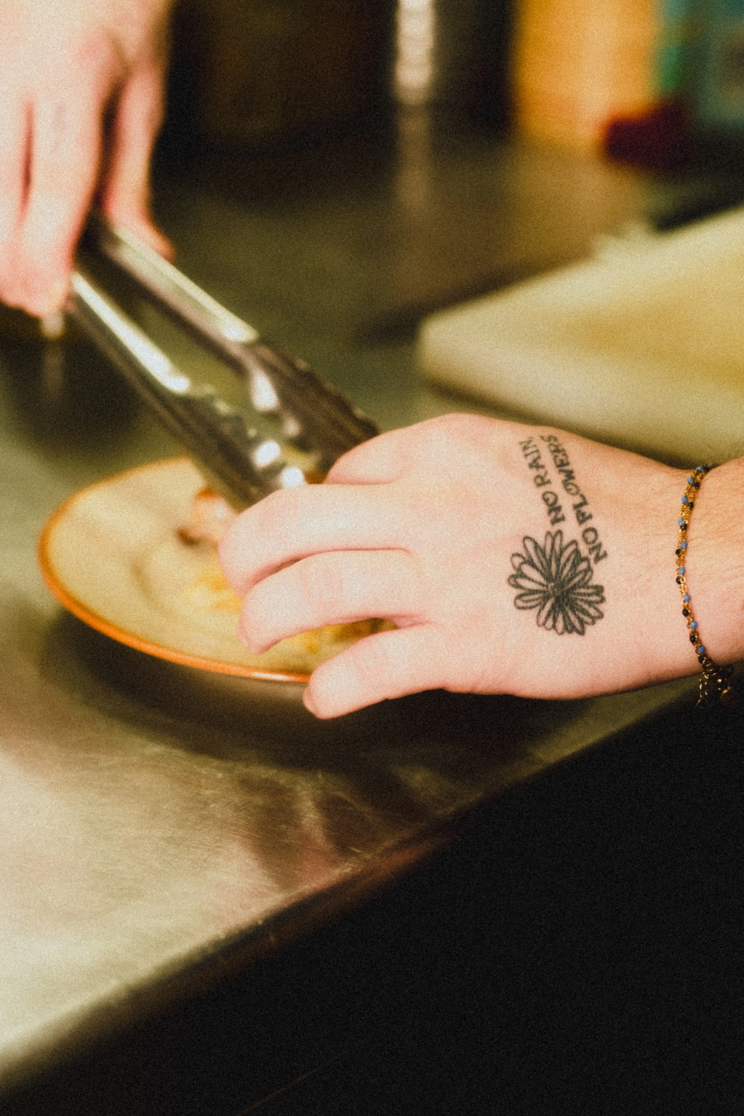 Person using tongs to pick slices from a peach on a small orange plate, with a tattoo and bracelet visible on their wrist.