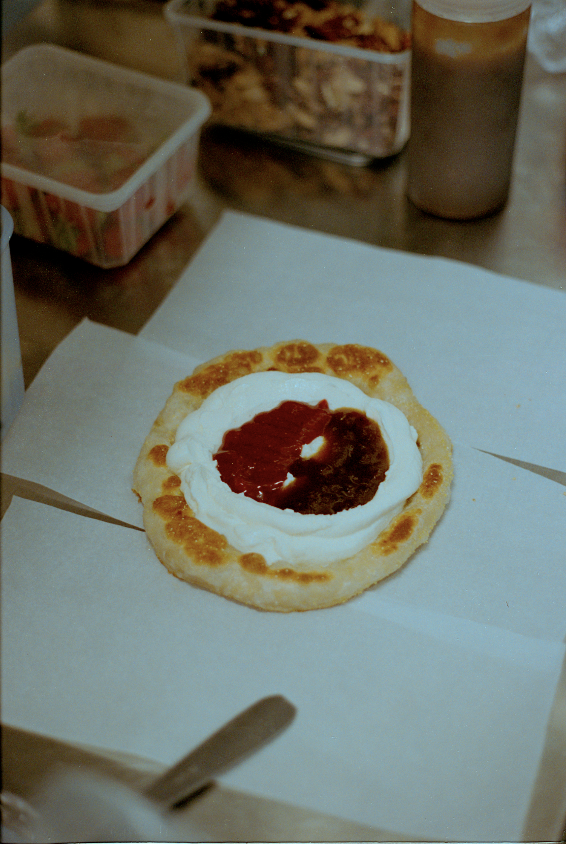 Un snack de pizza con queso mozzarella, salsa de tomate y pesto en una base de pan plano, sobre una hoja de papel de horno.