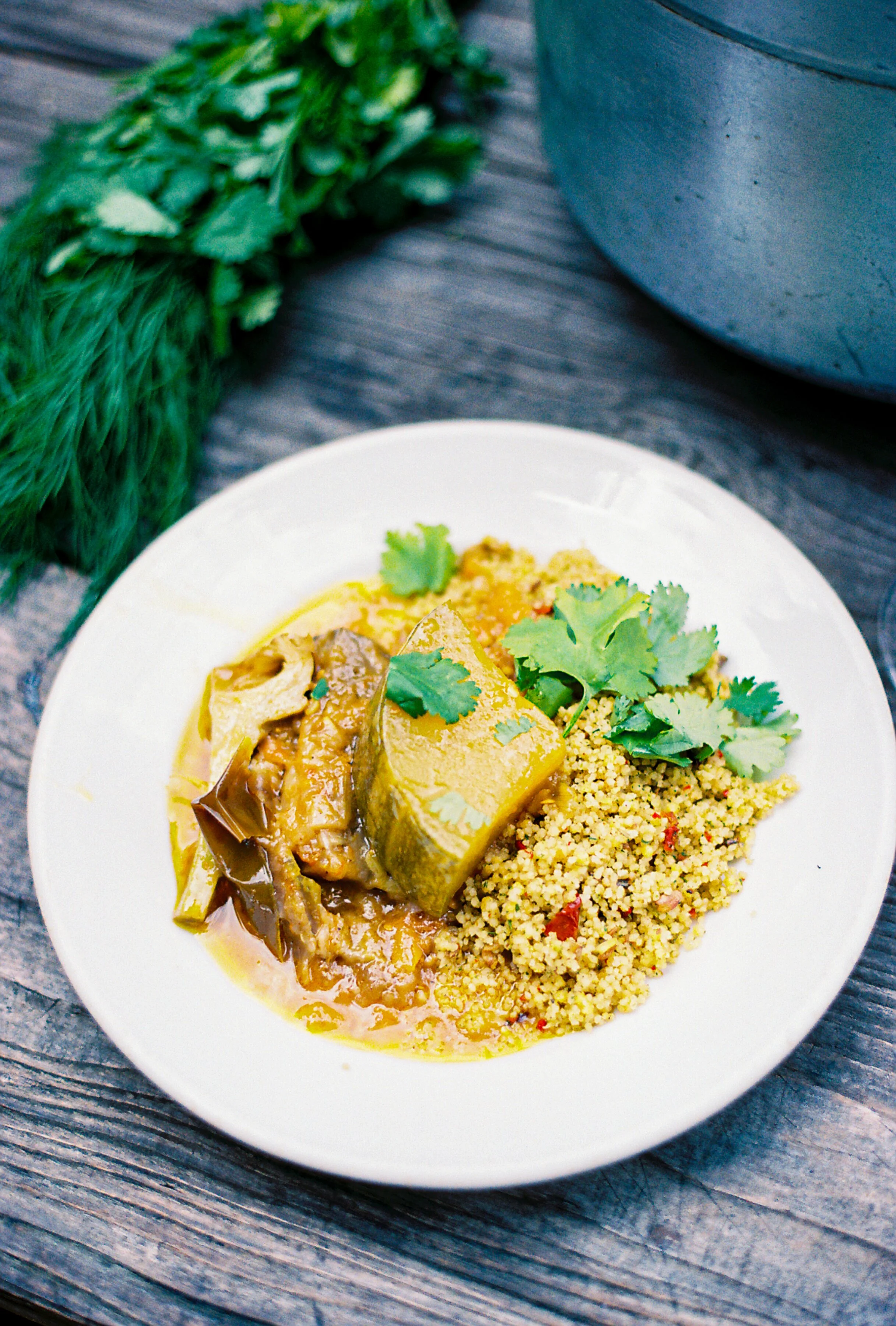 Plate of cooked seasoned rice, pumpkin, and a green curry with cilantro garnished on top, set on a rustic wooden table with greenery nearby.