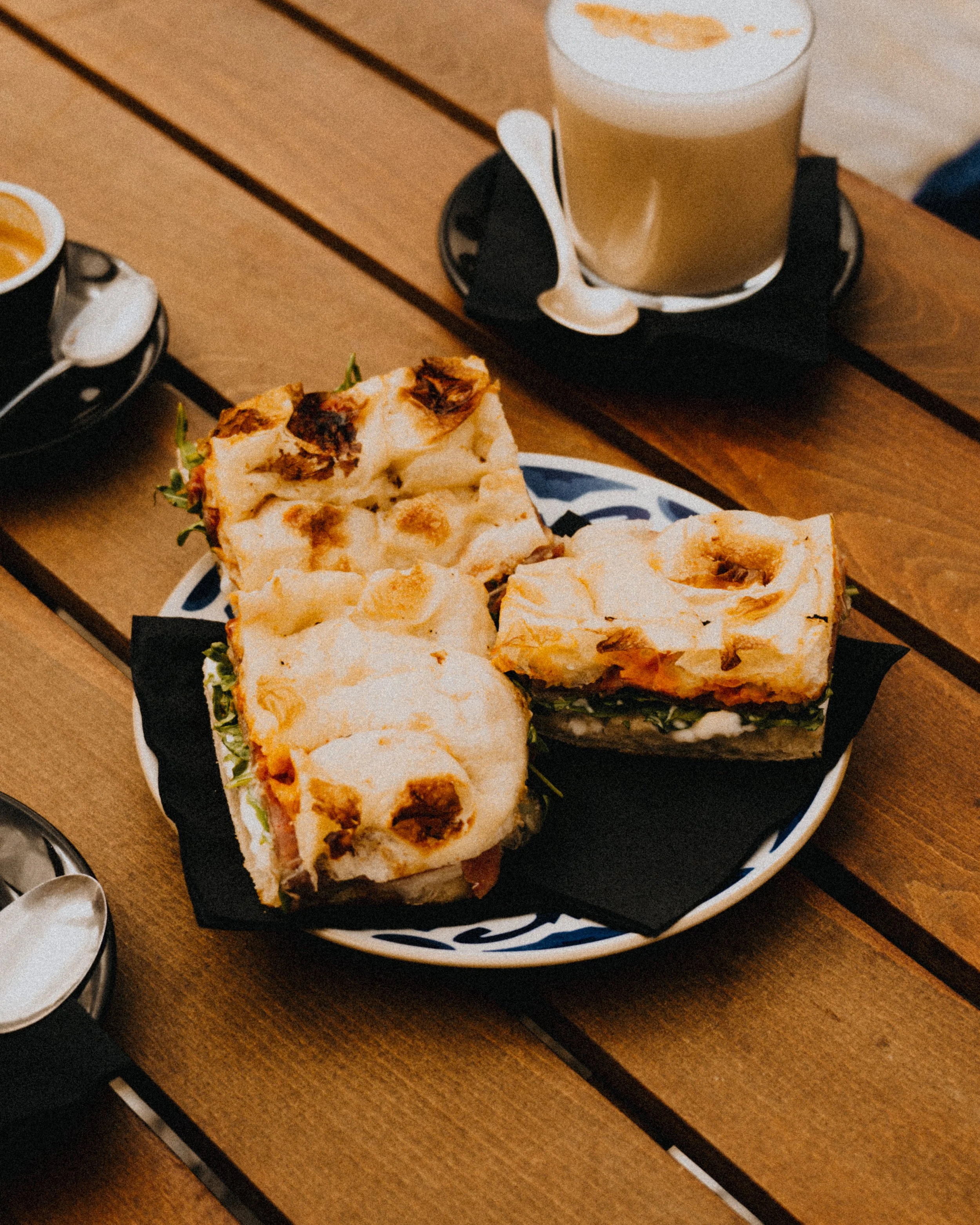 A plate with three slices of lasagna and two slices of pizza on a wooden table, with a glass of beer in the background.