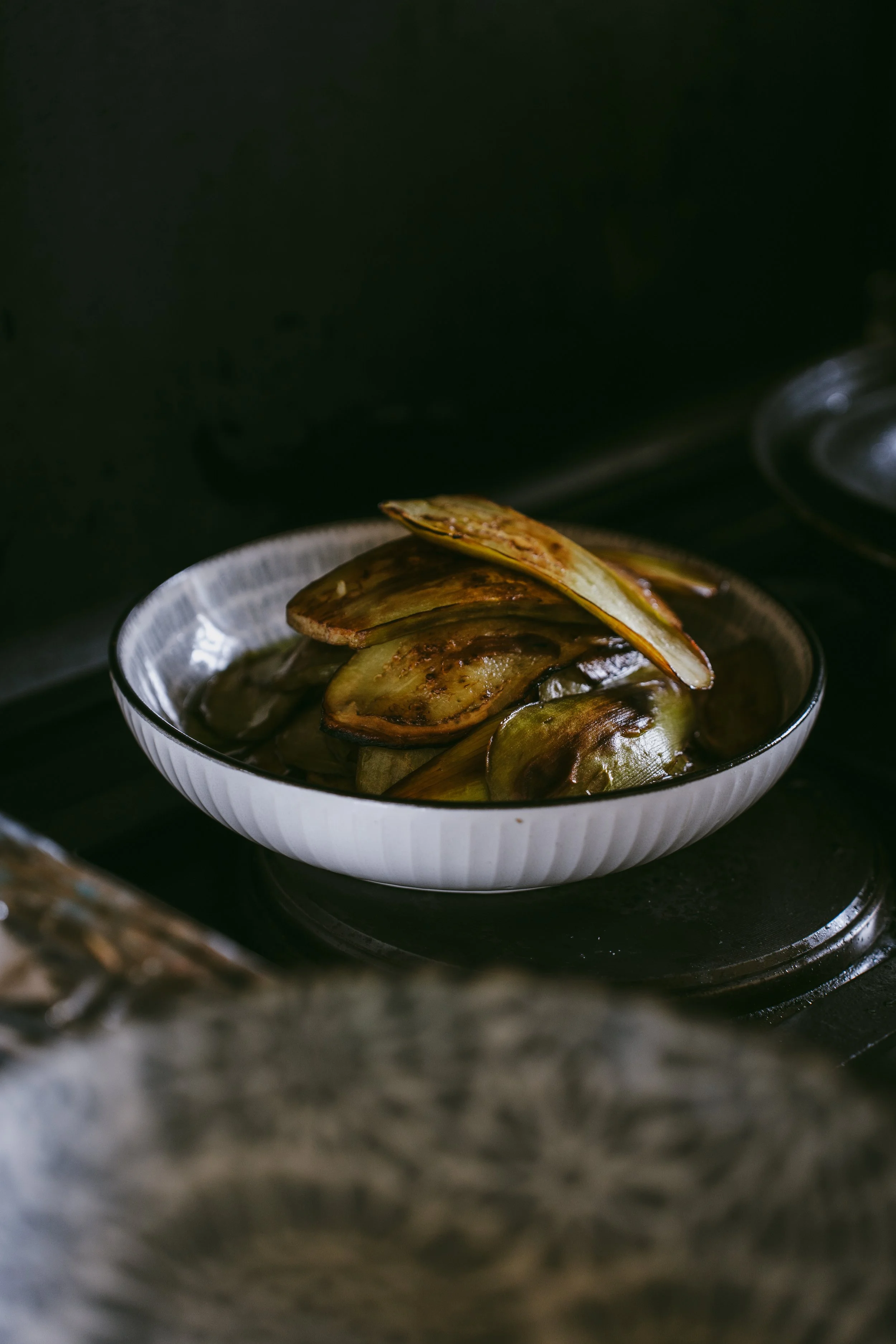 Slices of roasted eggplant in a white bowl on a stove.
