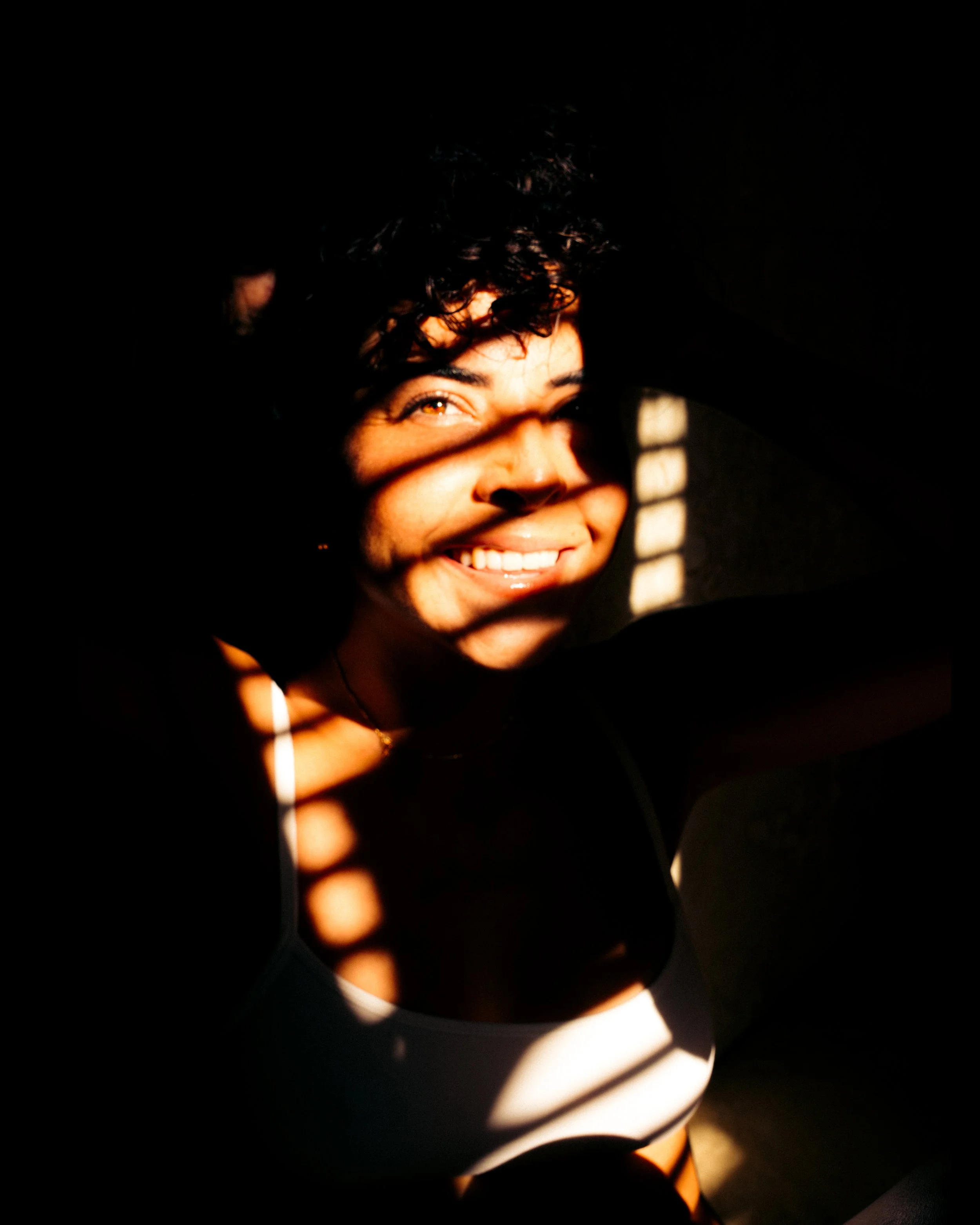 A young woman smiling with sunlight creating striped shadows across her face.