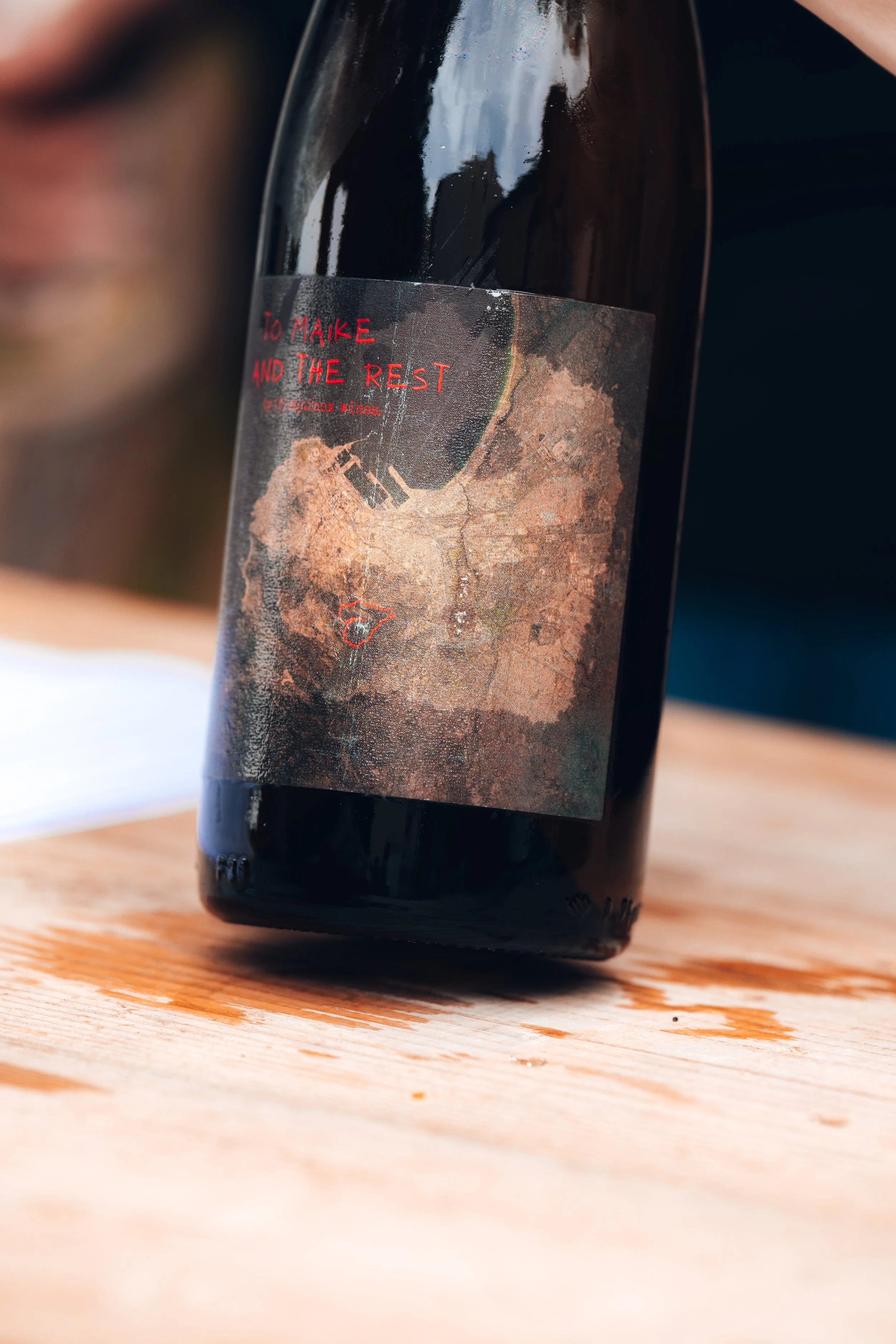 A bottle of wine with a label featuring a map and red text that says 'To Maike and the Rest'.