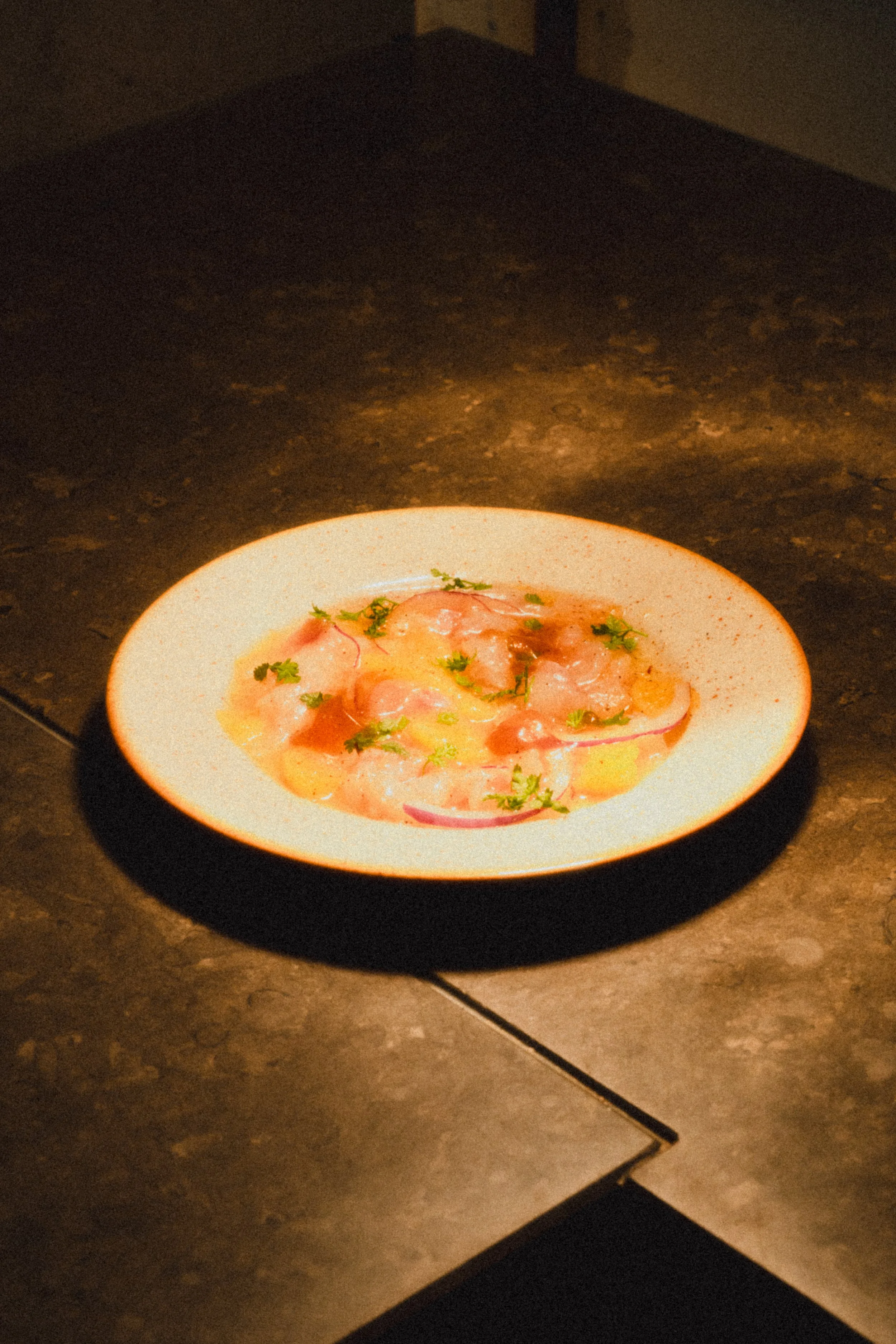 A white plate with a dish of raw, marinated eggs garnished with herbs, served on a dark, textured surface.
