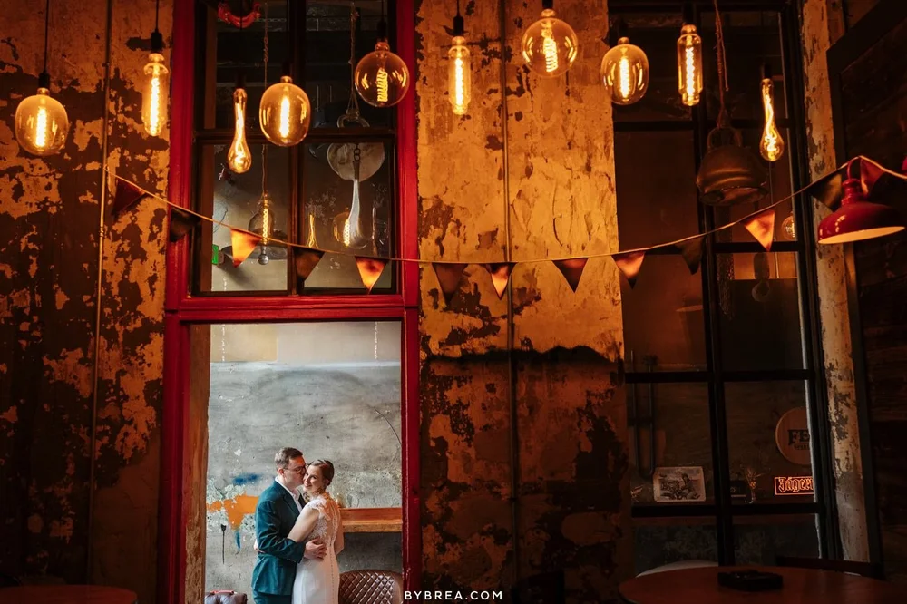 A couple framed by a red door under Edison bulbs at Guilford Hall