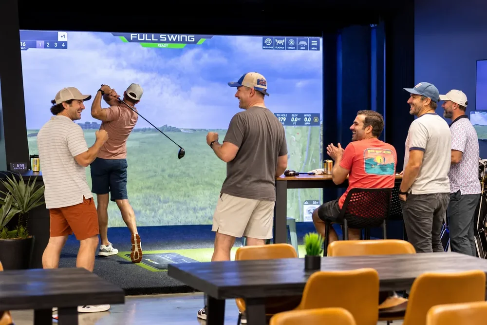A group cheering a drive in a Full Swing simulator bay