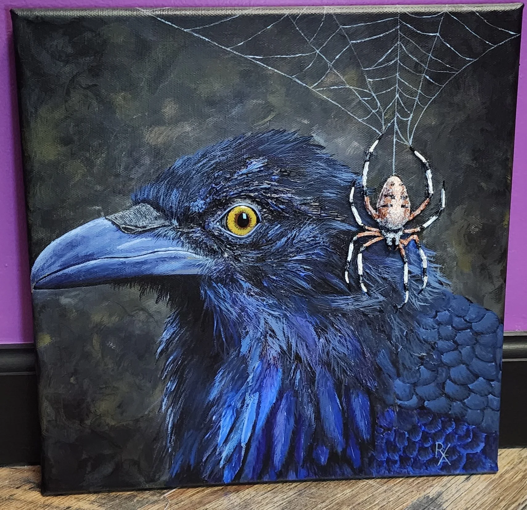 A painting of a blue-black ravens head with a yellow eye, with a spider hanging from a web above it.