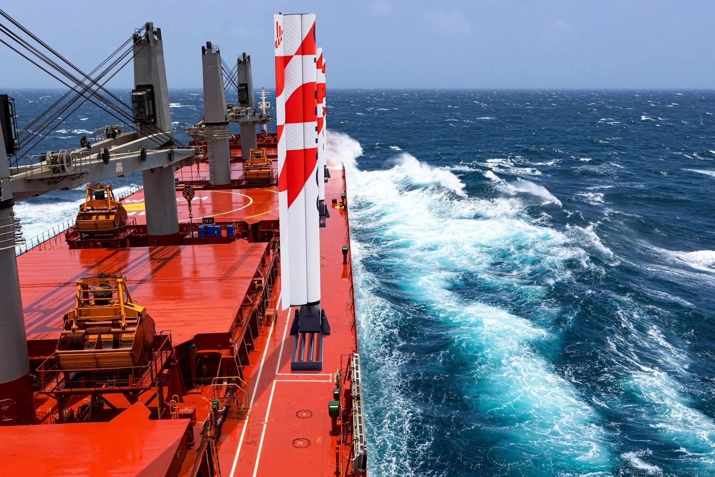 A view from the deck of a red oil tanker ship sailing in the ocean with white waves and a cloudy sky.