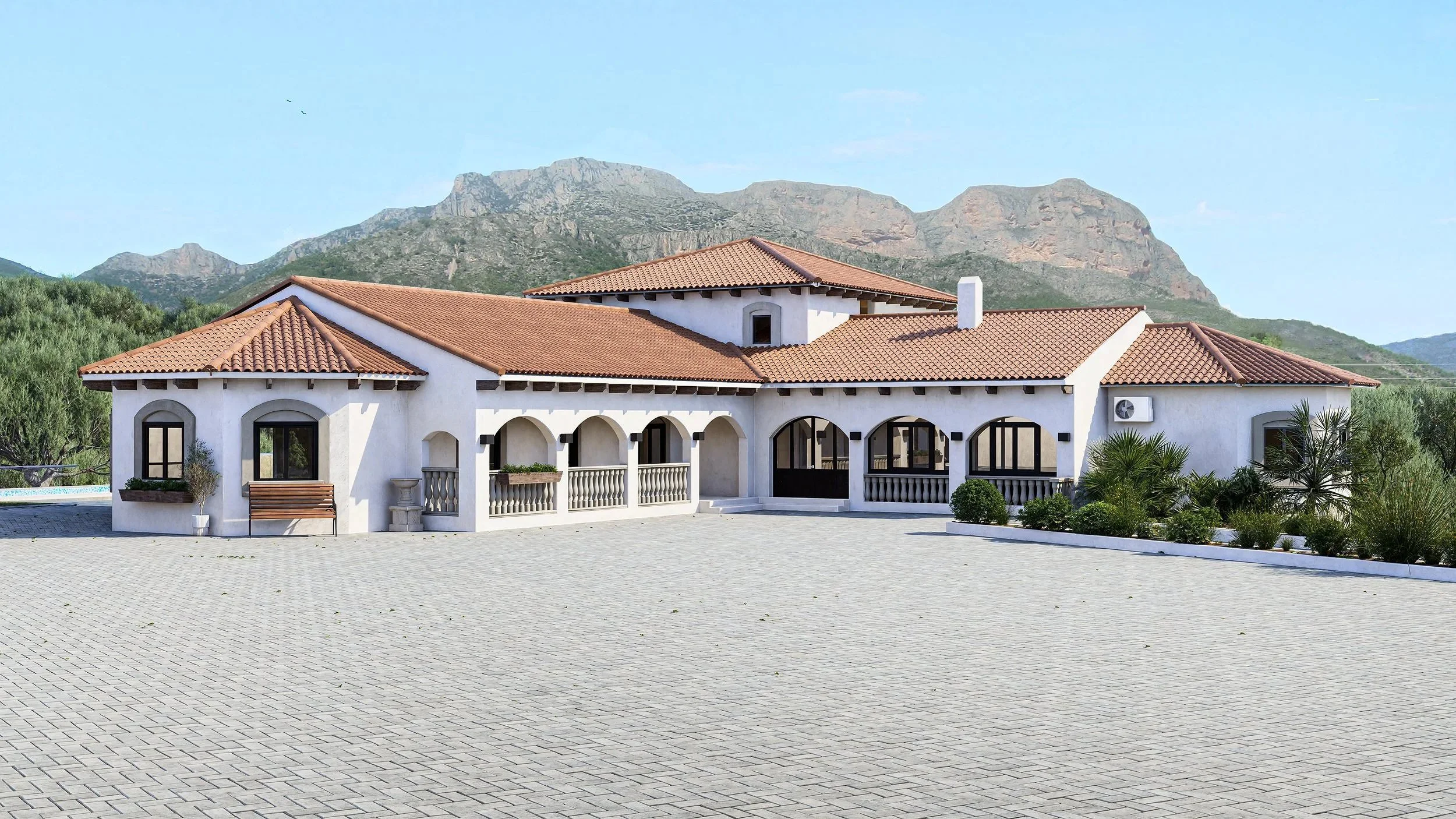 A large white house with a red-tiled roof, arched windows, and a spacious paved courtyard, set against a mountainous landscape.