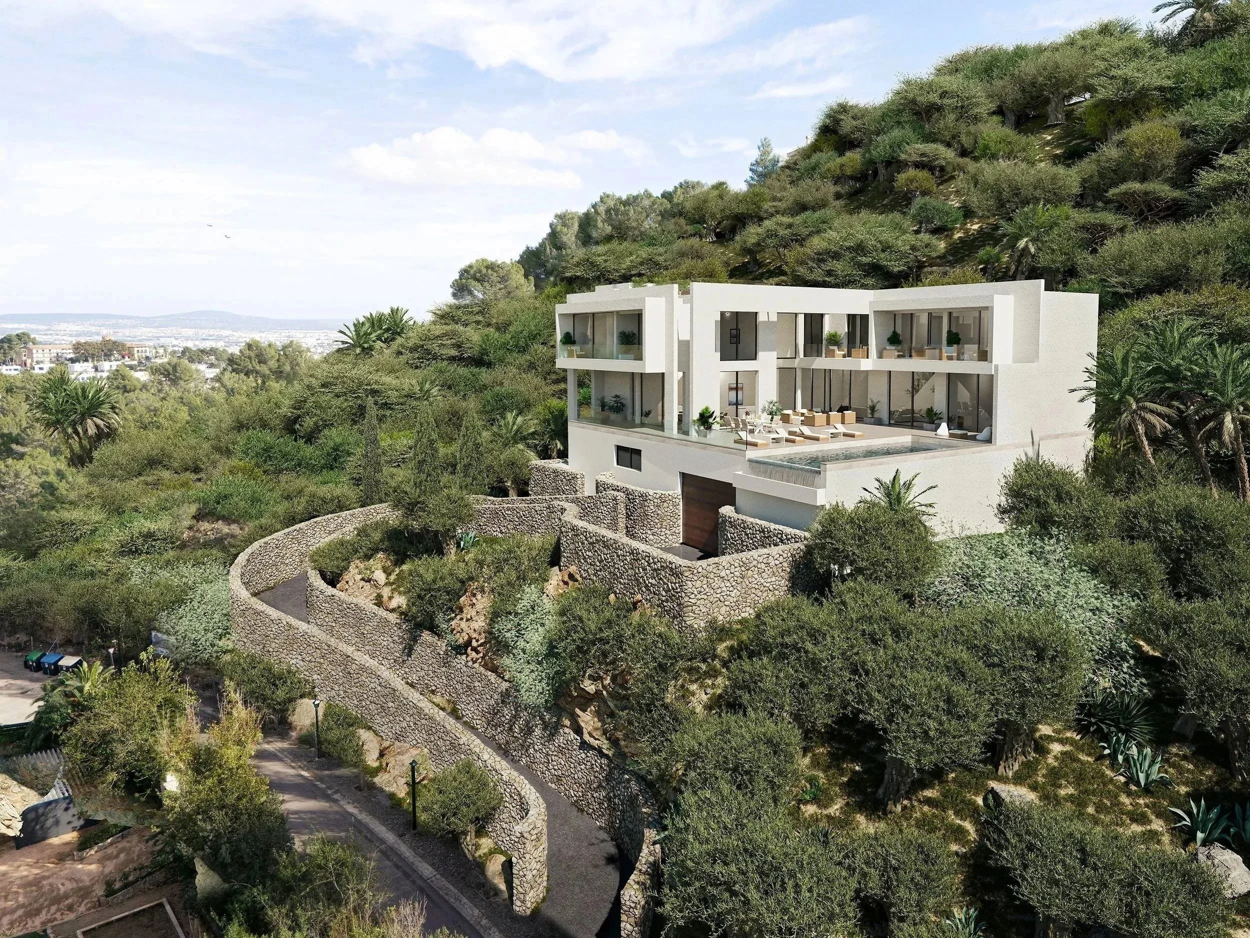 Modern white house with large glass windows and balconies, built into a hillside surrounded by green trees and plants, featuring a curved stone retaining wall and a pool area.