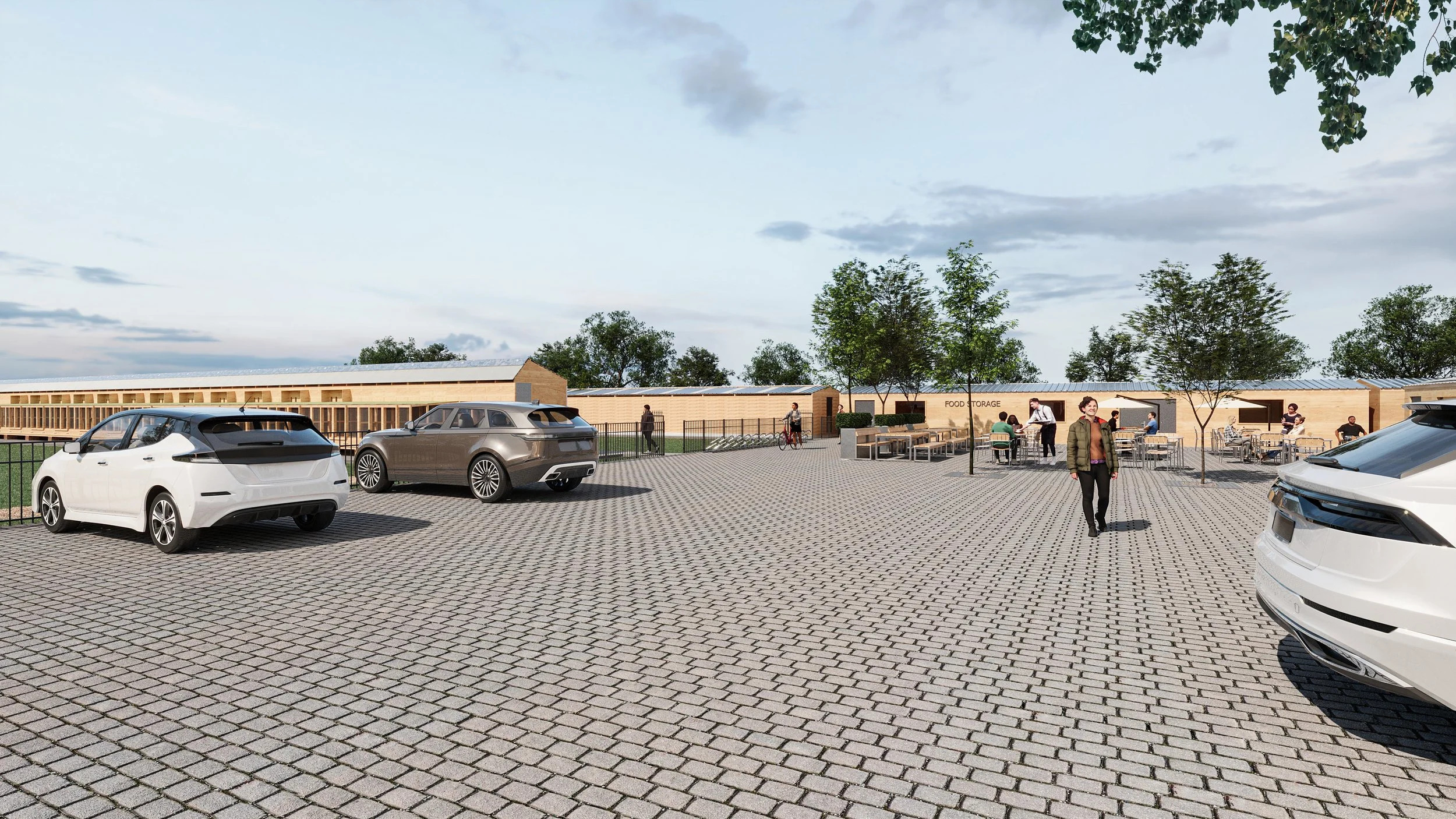 A parking lot with white and gray cars, trees, a food storage area, and people sitting at outdoor tables.