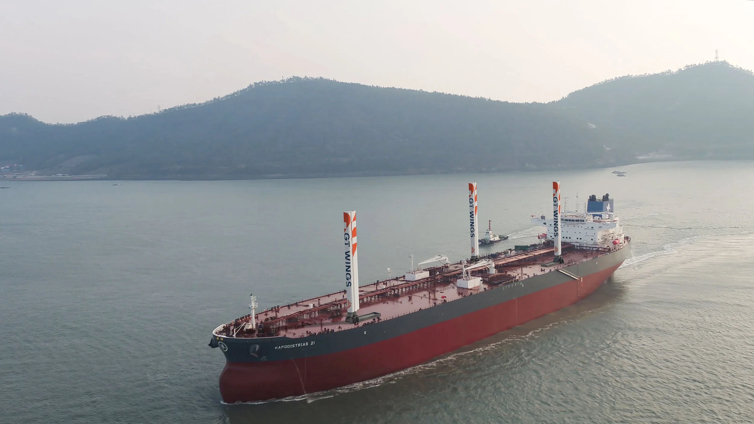 A large oil tanker with the name 'Kapodistrias 21' on its bow, sailing in calm water with hills in the background.