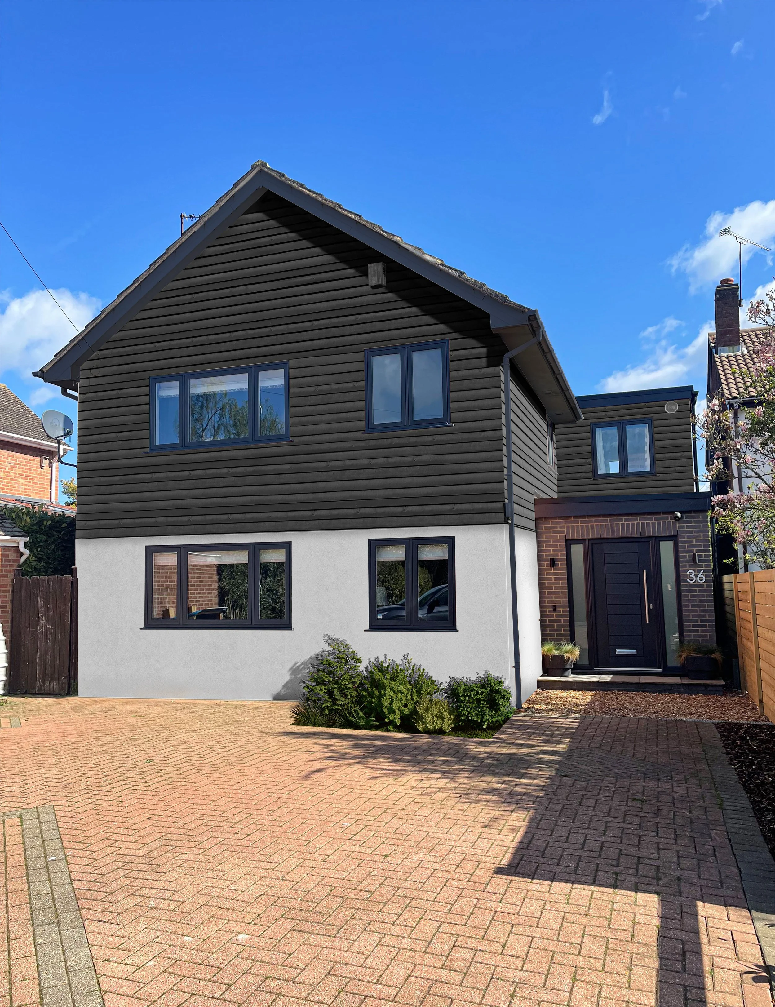 Modern residential house with black wooden and white exterior, multiple windows, a black front door, and a brick driveway under a blue sky.