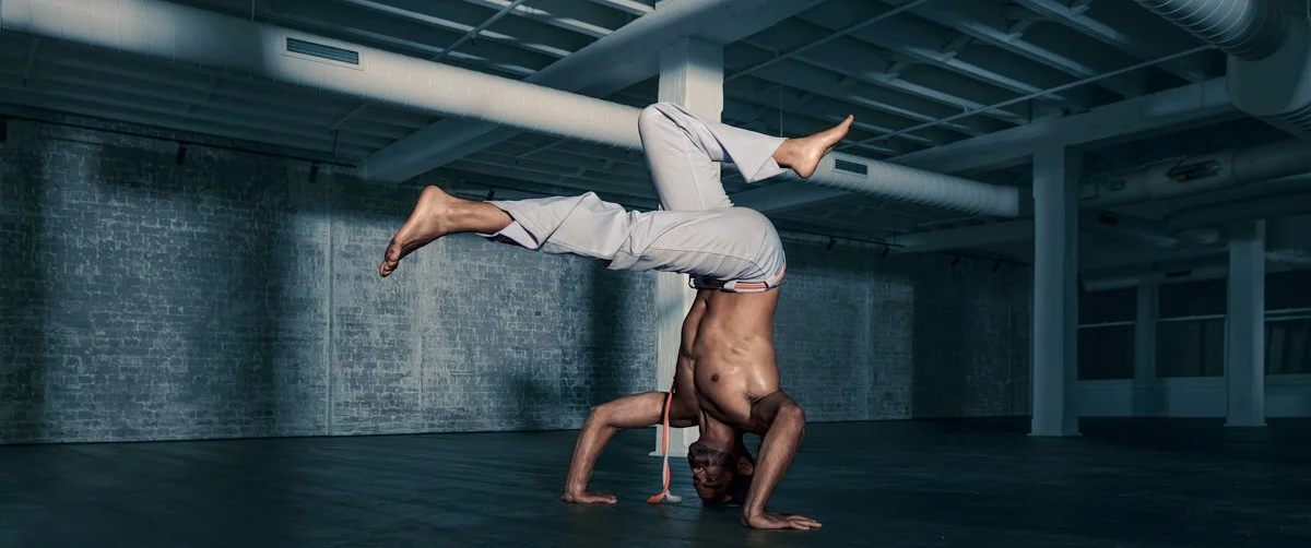 A shirtless man performing a headstand yoga pose in a spacious, industrial-style room.