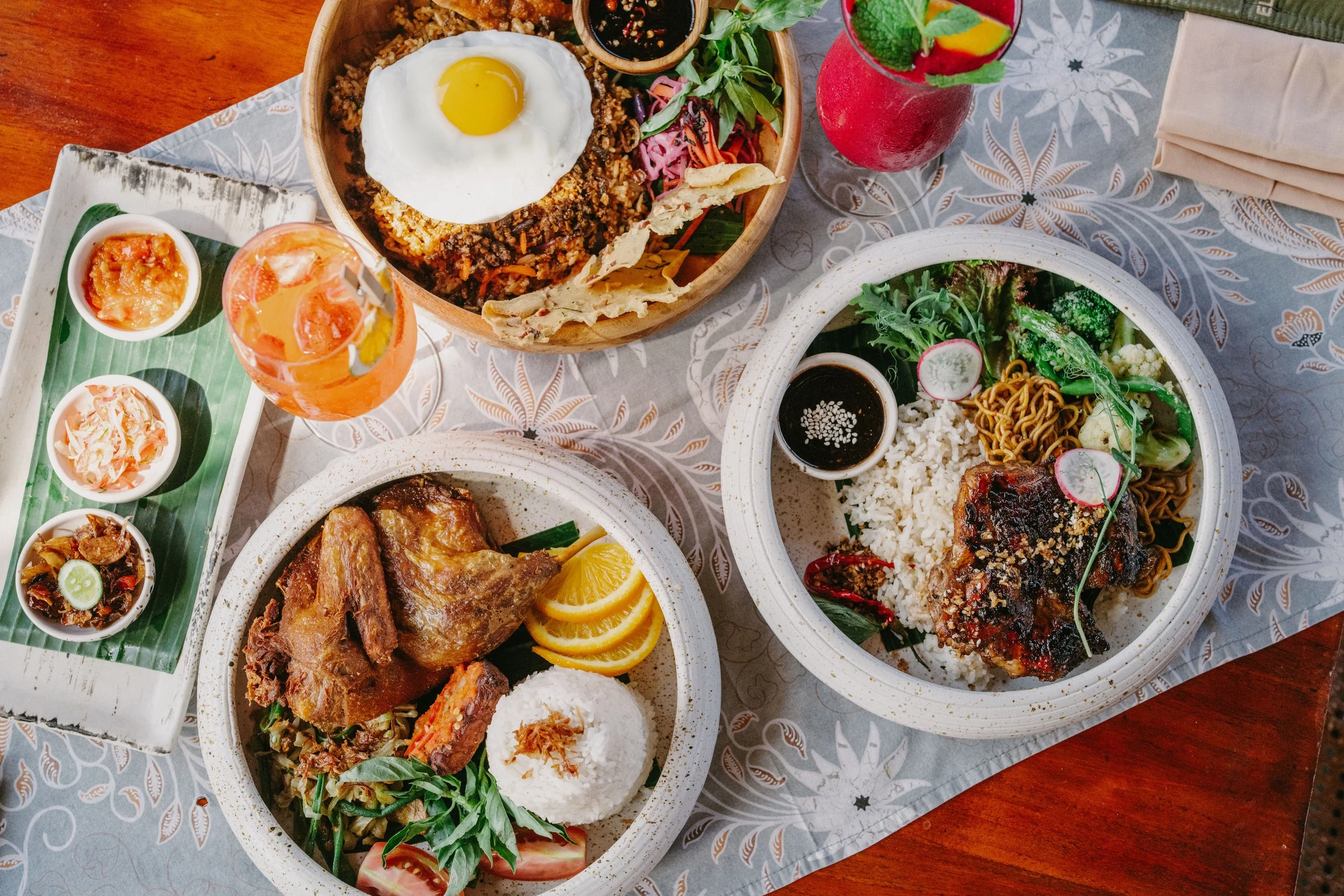 A table with Thai cuisine dishes, including rice, grilled meat, noodles, vegetables, condiments, and colorful drinks.