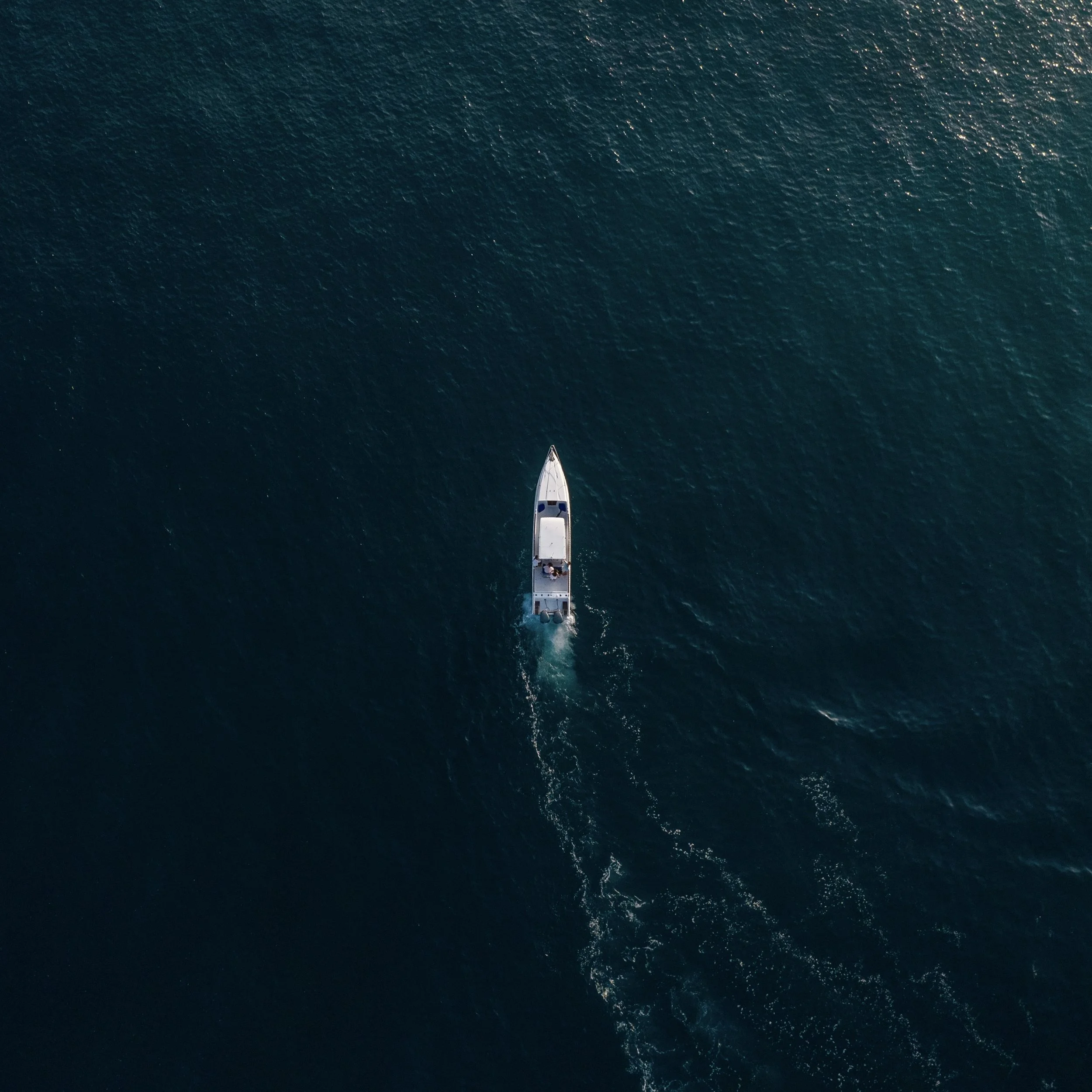 Aerial view of a boat cruising through calm blue water, leaving a trail of waves behind.