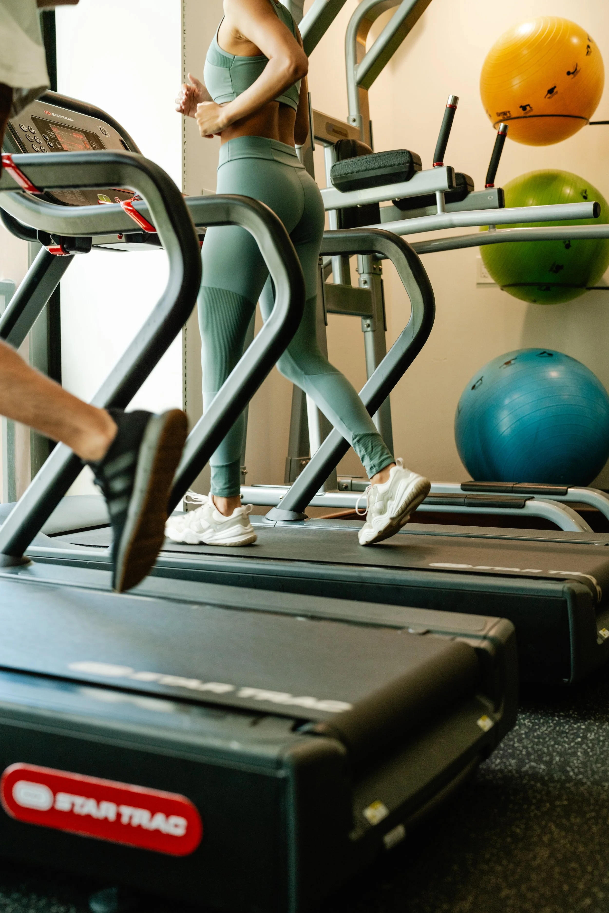 People running on treadmills in a gym, with exercise balls mounted on the wall behind them.